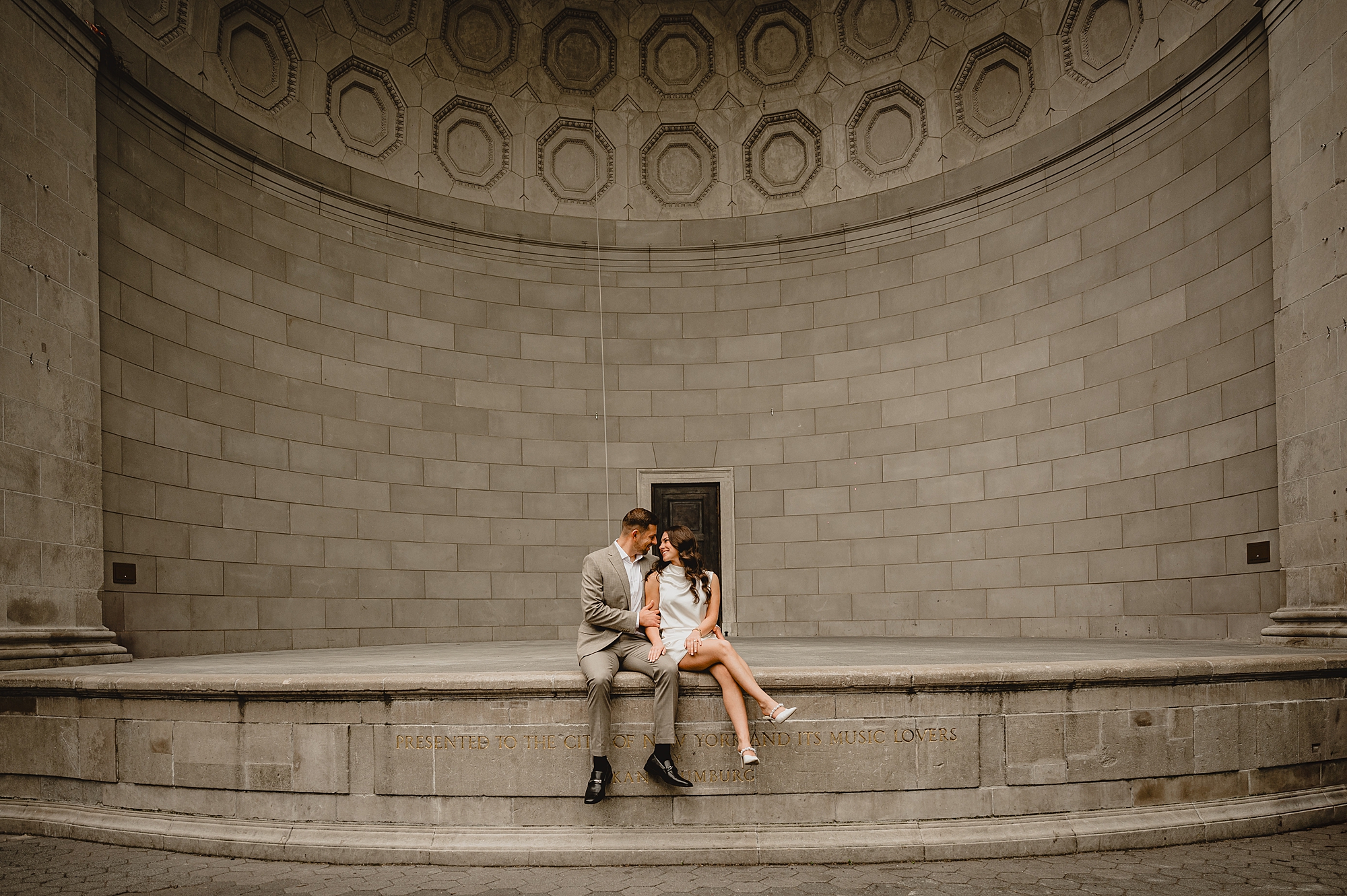 engaged couple sits on stone wall inside Central Park