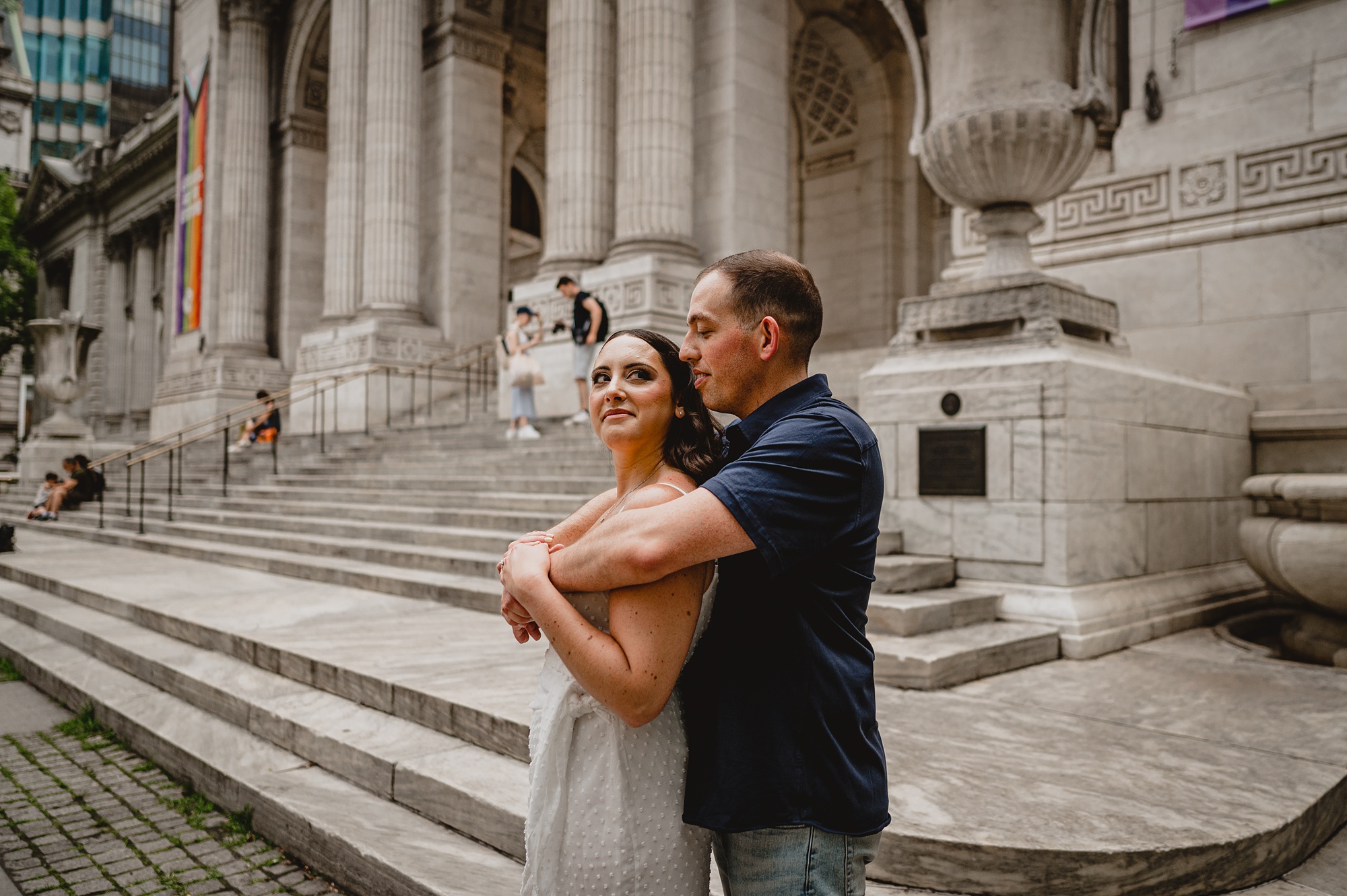 man hugs fiancee on steps of the New York Public Library