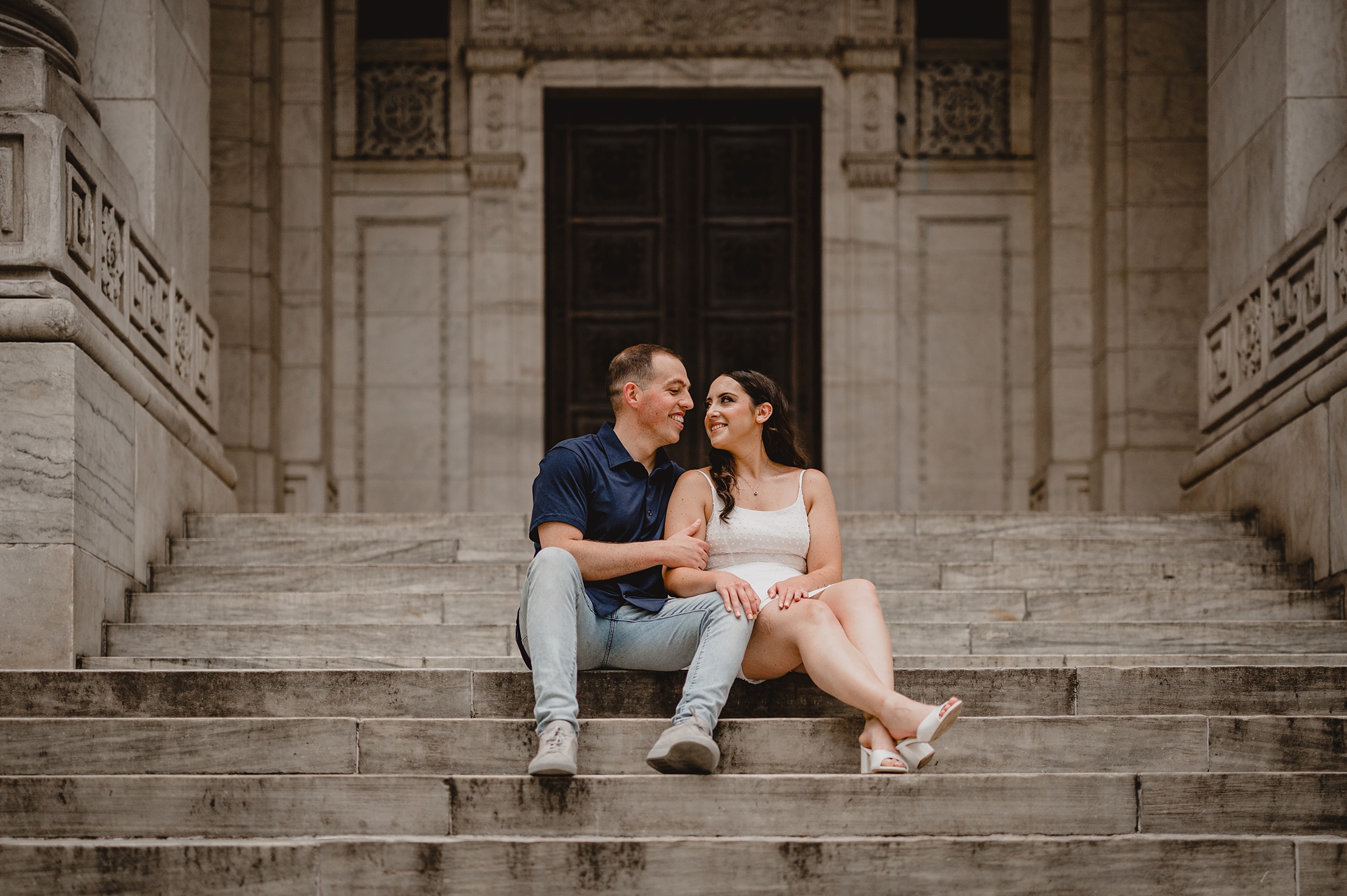 engaged couple sits on steps of New York Public Library