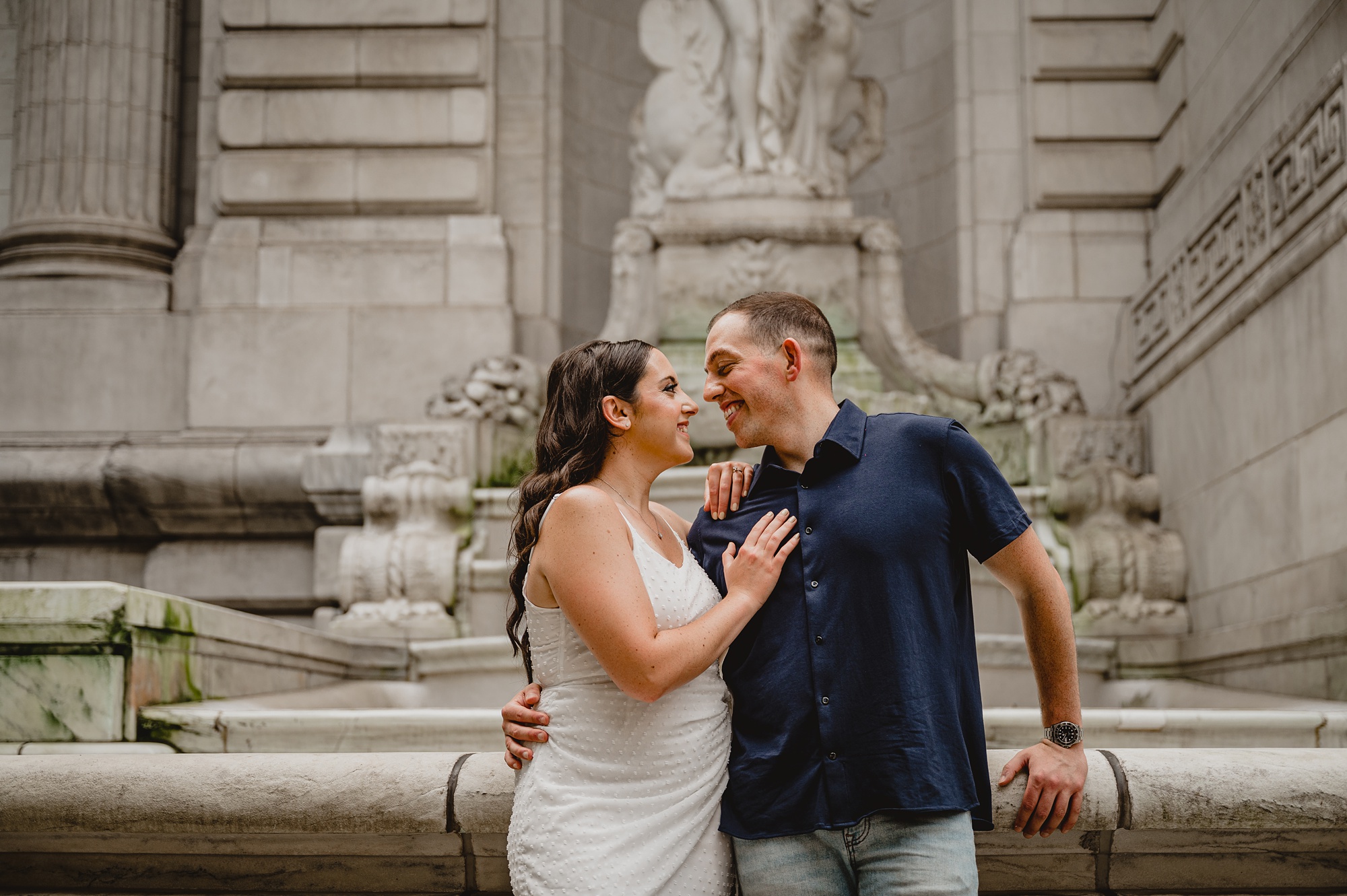 engaged couple hugs by statues outside New York Public Library