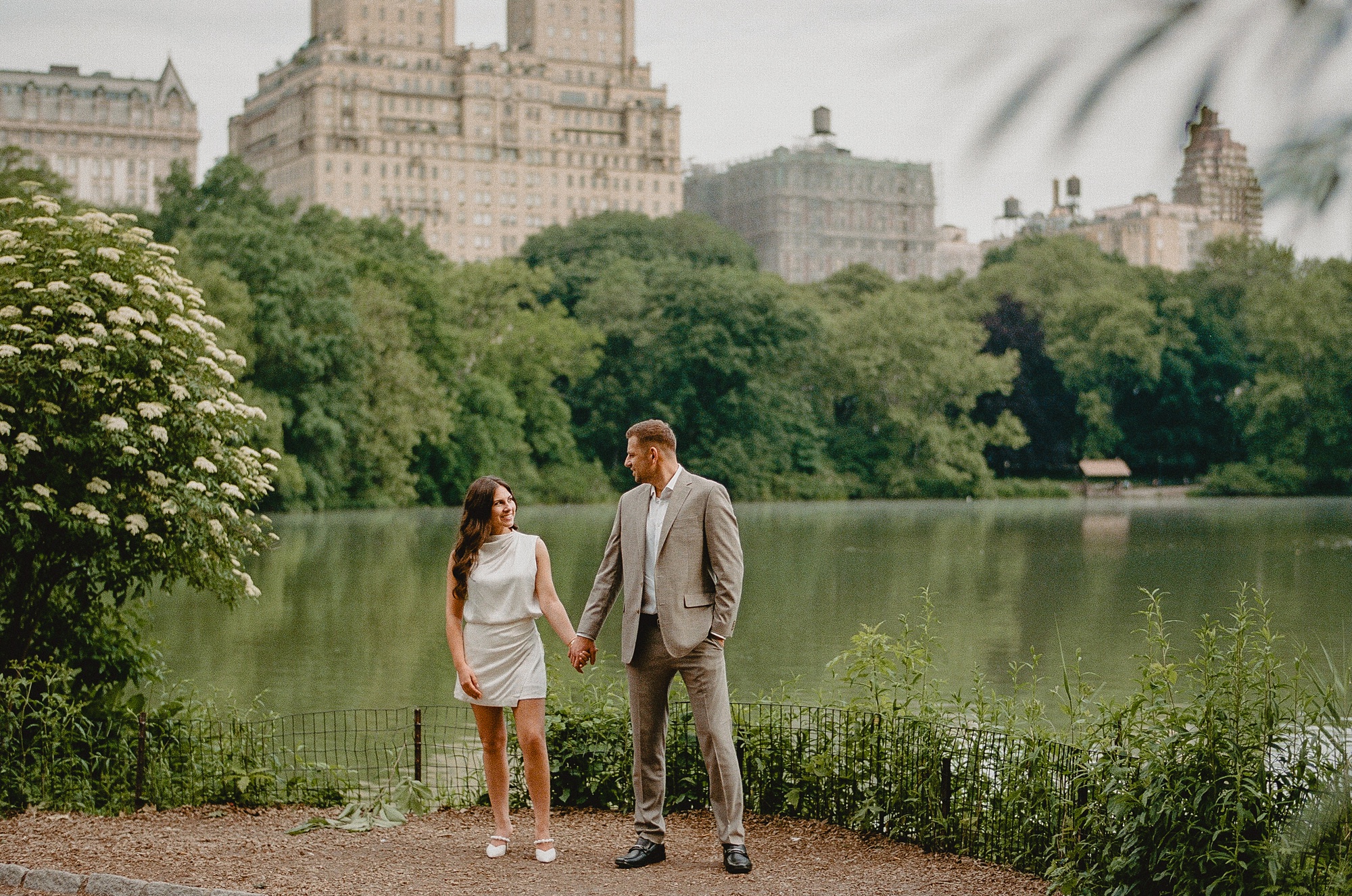 engaged couple holds hands in front of pond in Central Park