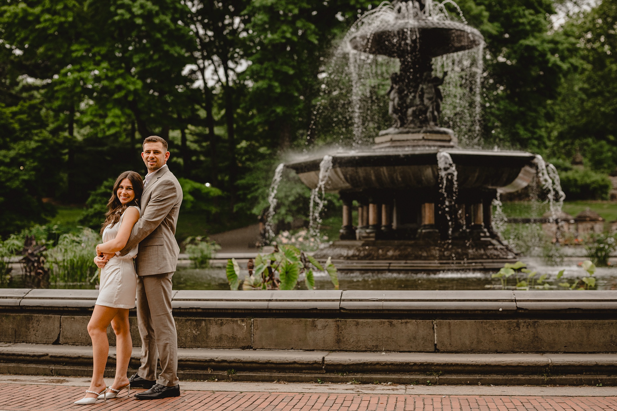engaged couple hugs in front of Bethesda fountain in Central Park