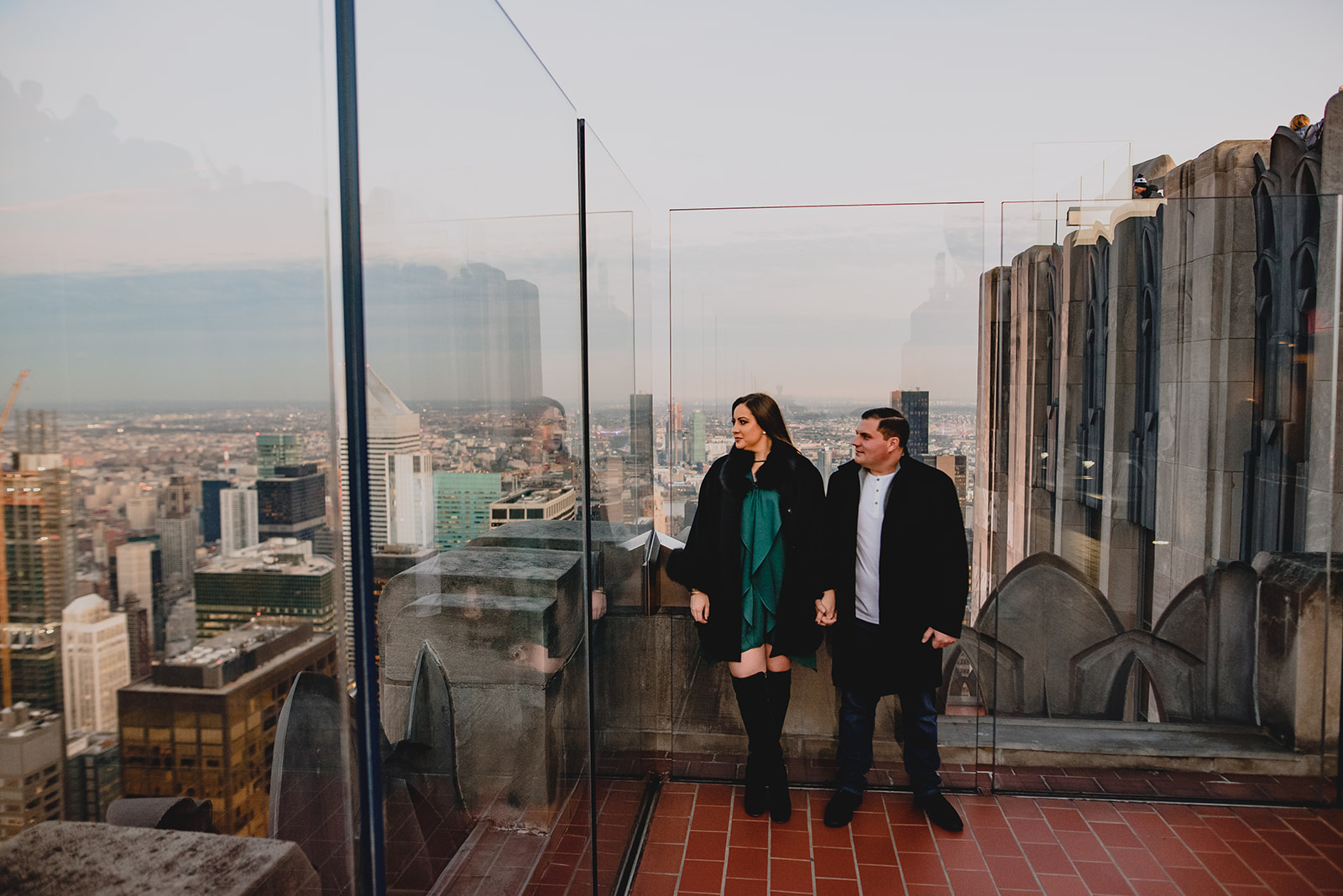 man and woman hold hands leaning against glass walls of Top of the Rock