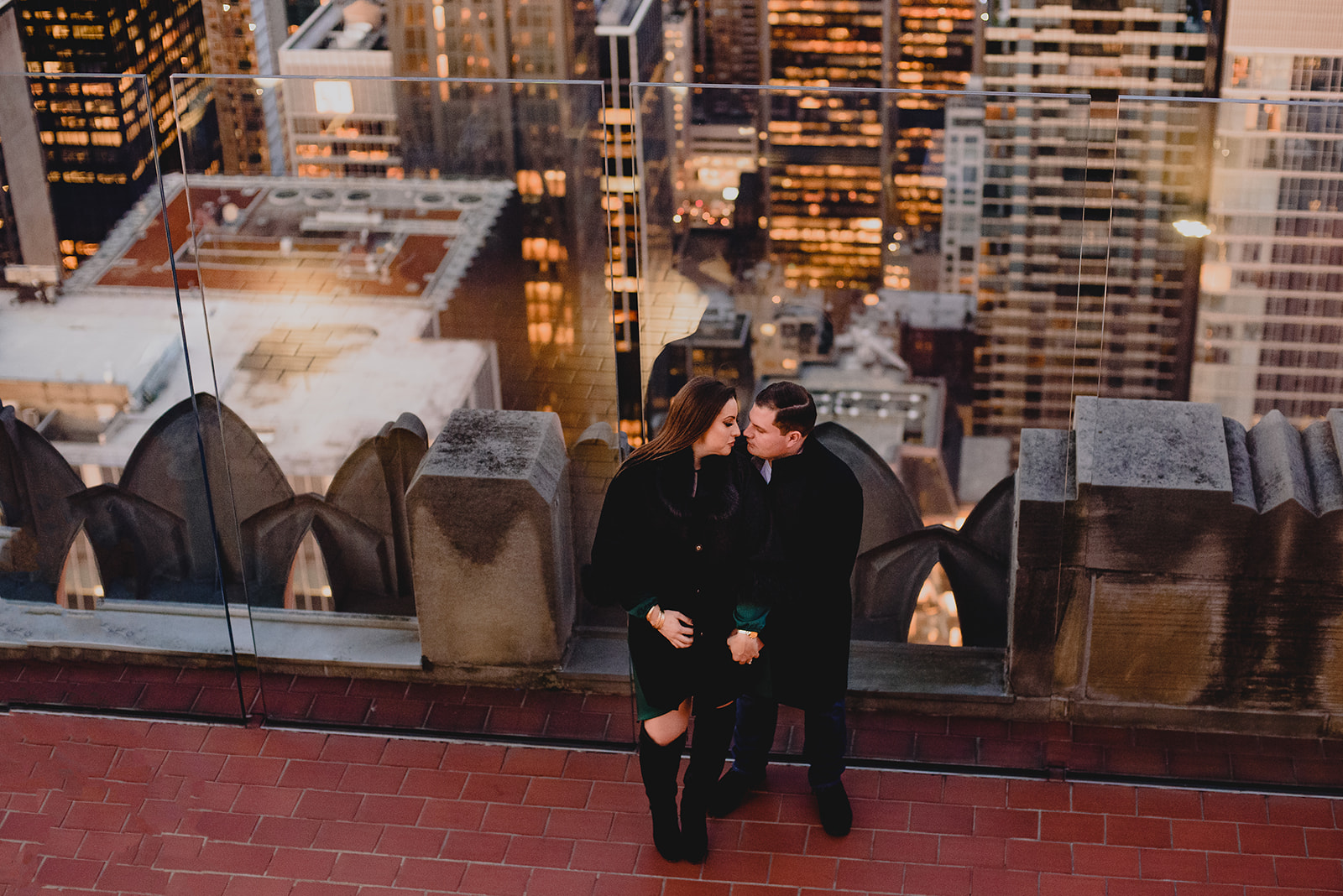 engaged couple leans against glass walls at Top of the Rock overlook