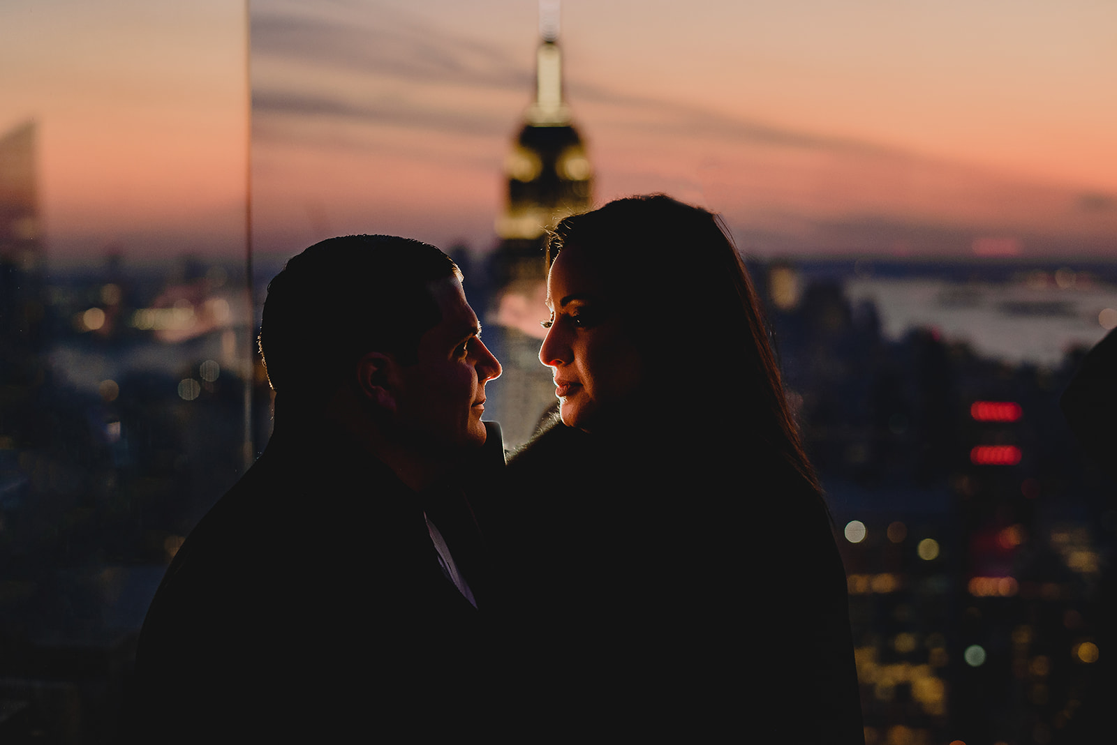 couple hugs at sunset with NYC skyline behind them