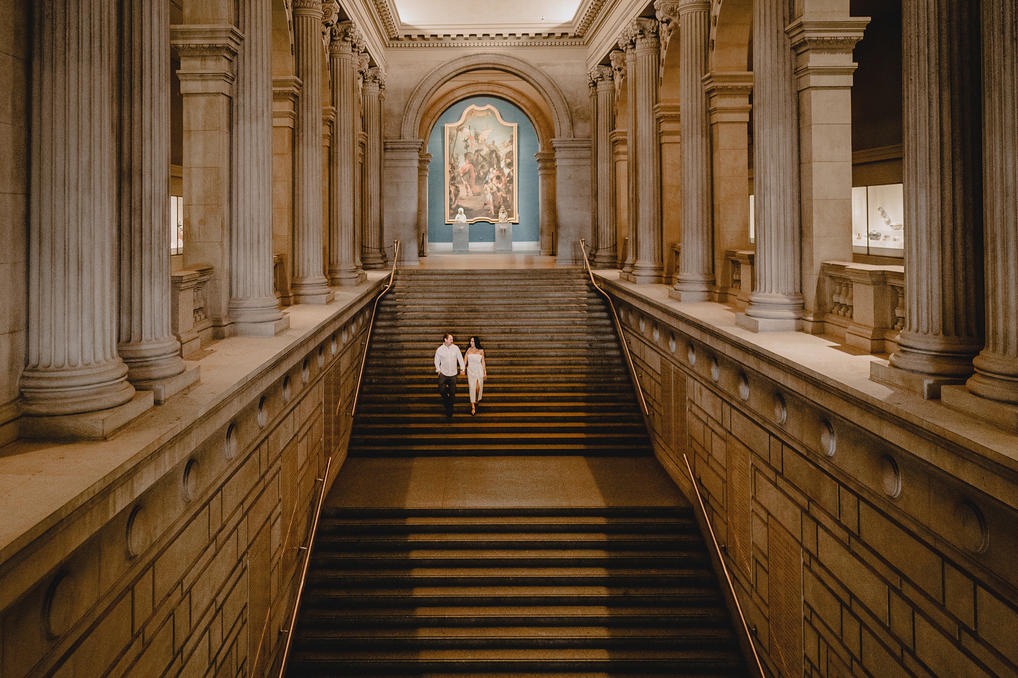 man and woman walk down steps of the Met holding hands during engagement photos