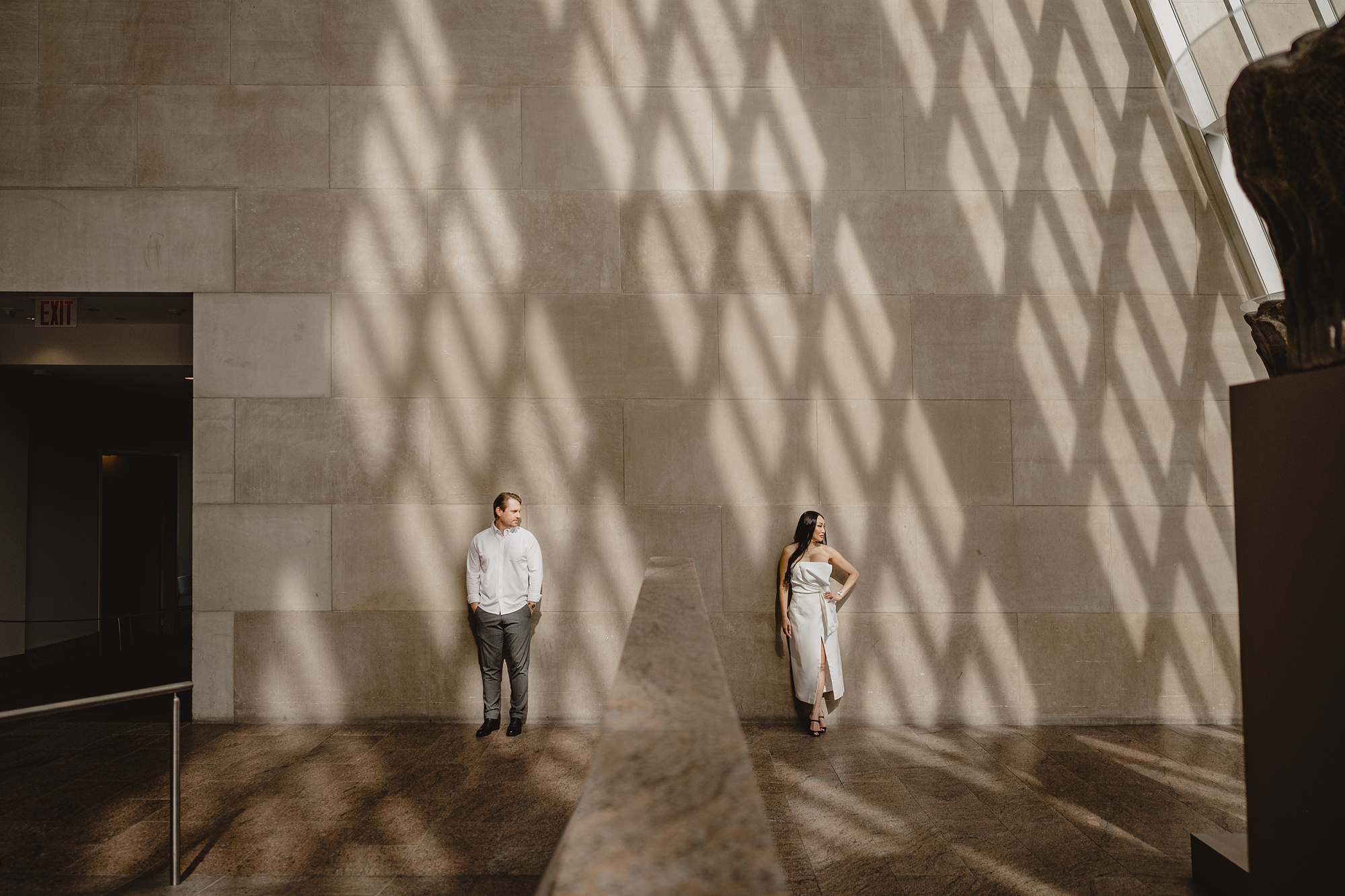 man and woman lean against wall of the Met with crisscross shadow