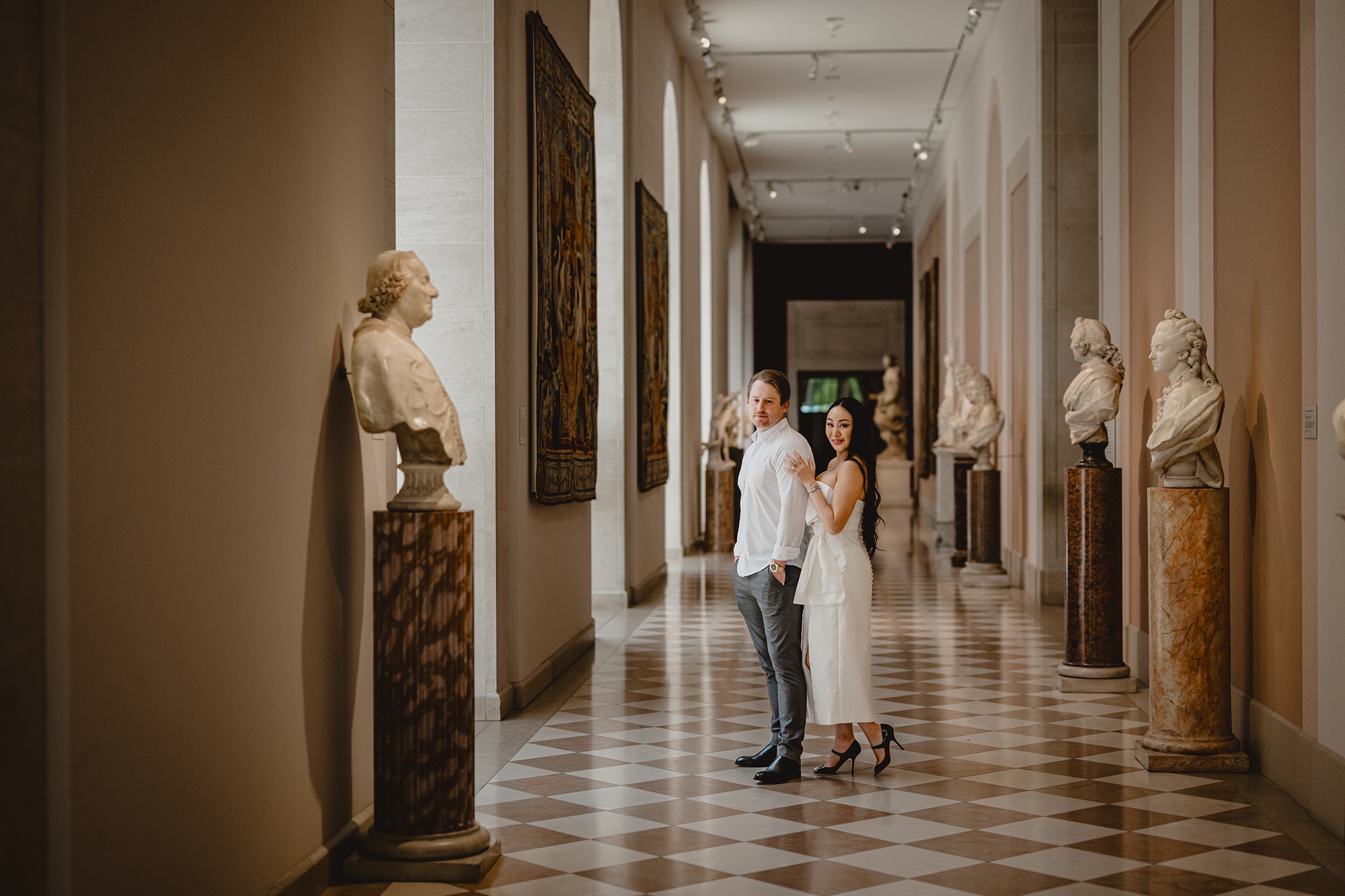 woman in white dress hugs man from behind in hallway of the Met
