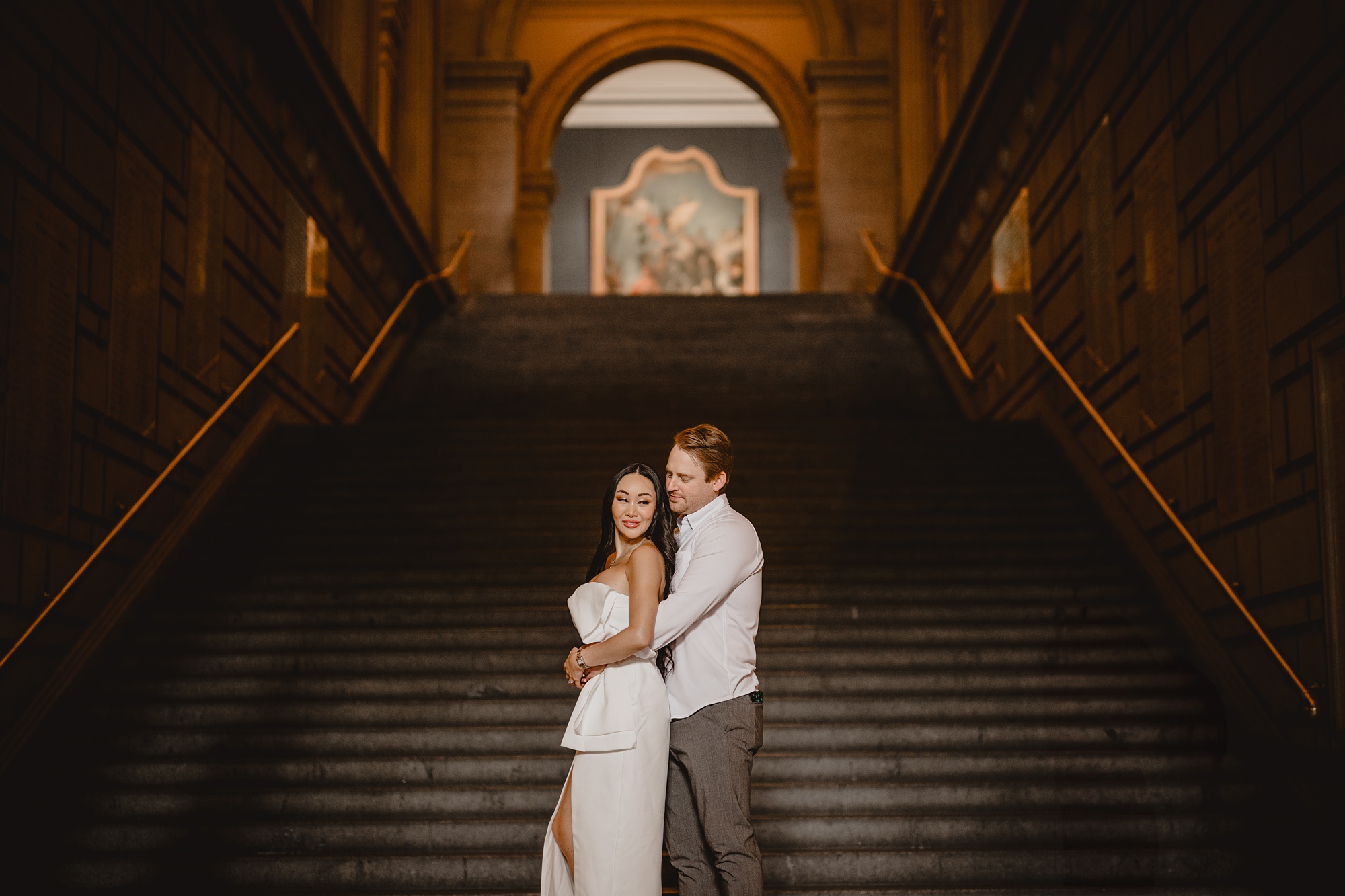 man hugs woman from behind on staircase inside the Met