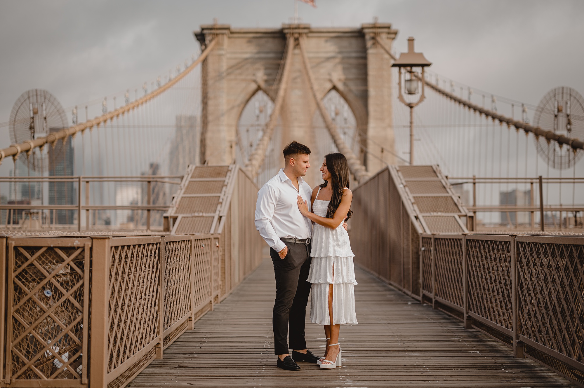 engaged couple stands on Brooklyn Bridge in New York City