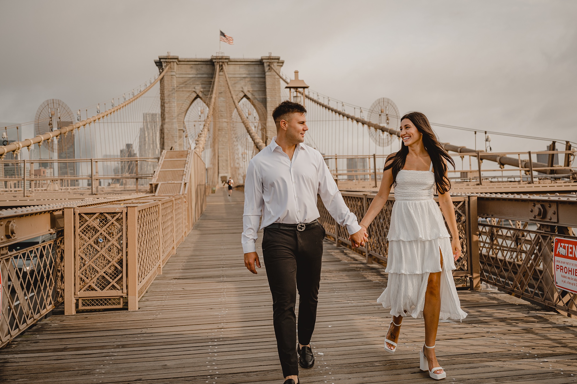engaged couple holds hands walking across the Brooklyn Bridge