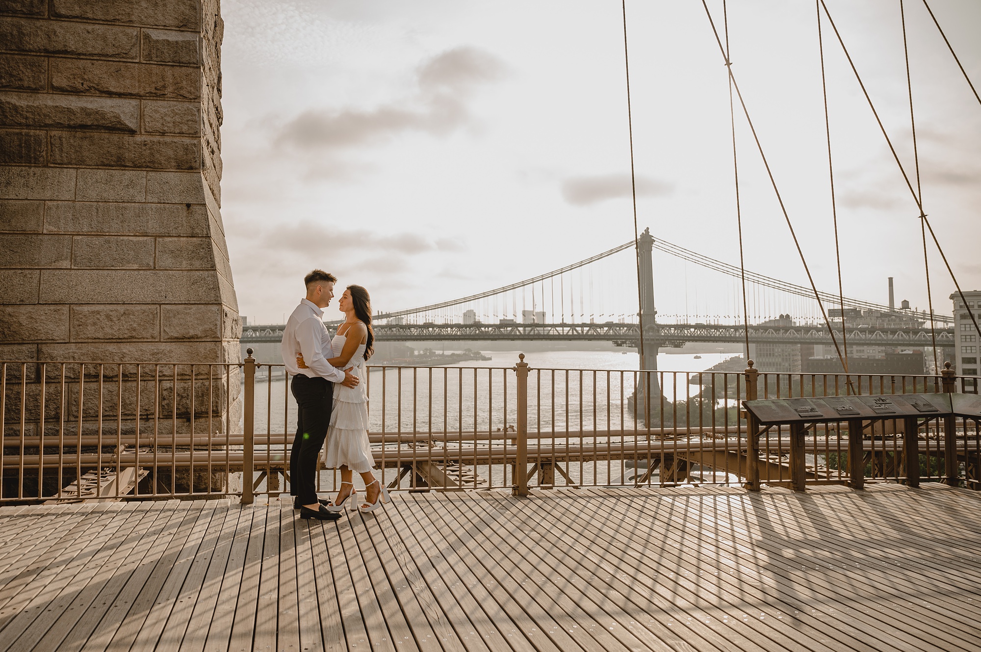 engaged couple hugs on the Brooklyn Bridge at sunset