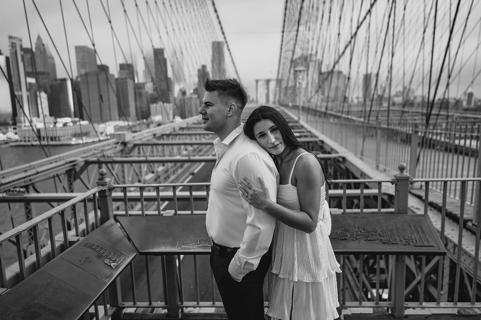 woman leans on man's back standing on the Brooklyn Bridge