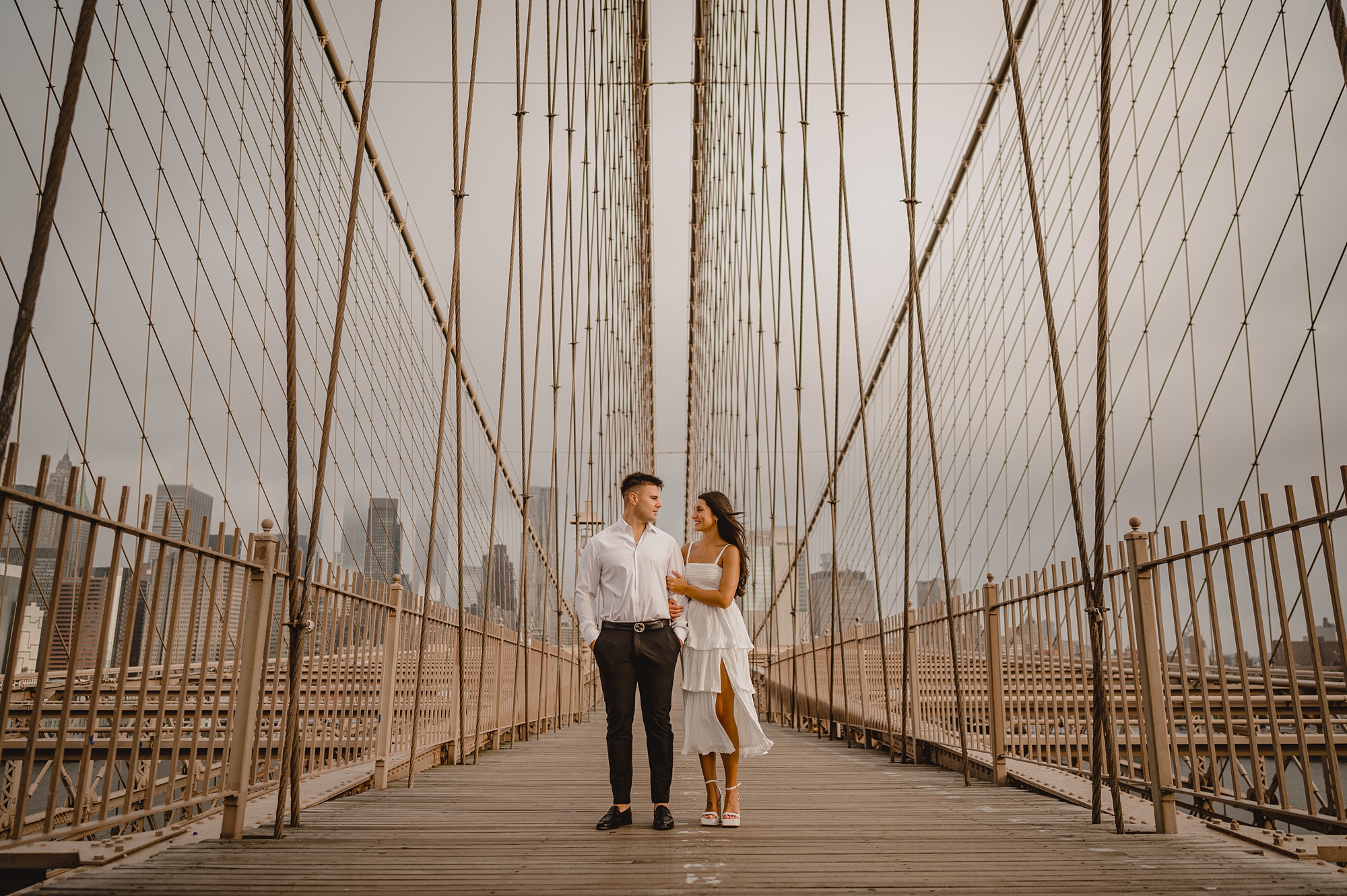 engaged couple stands on the Brooklyn Bridge