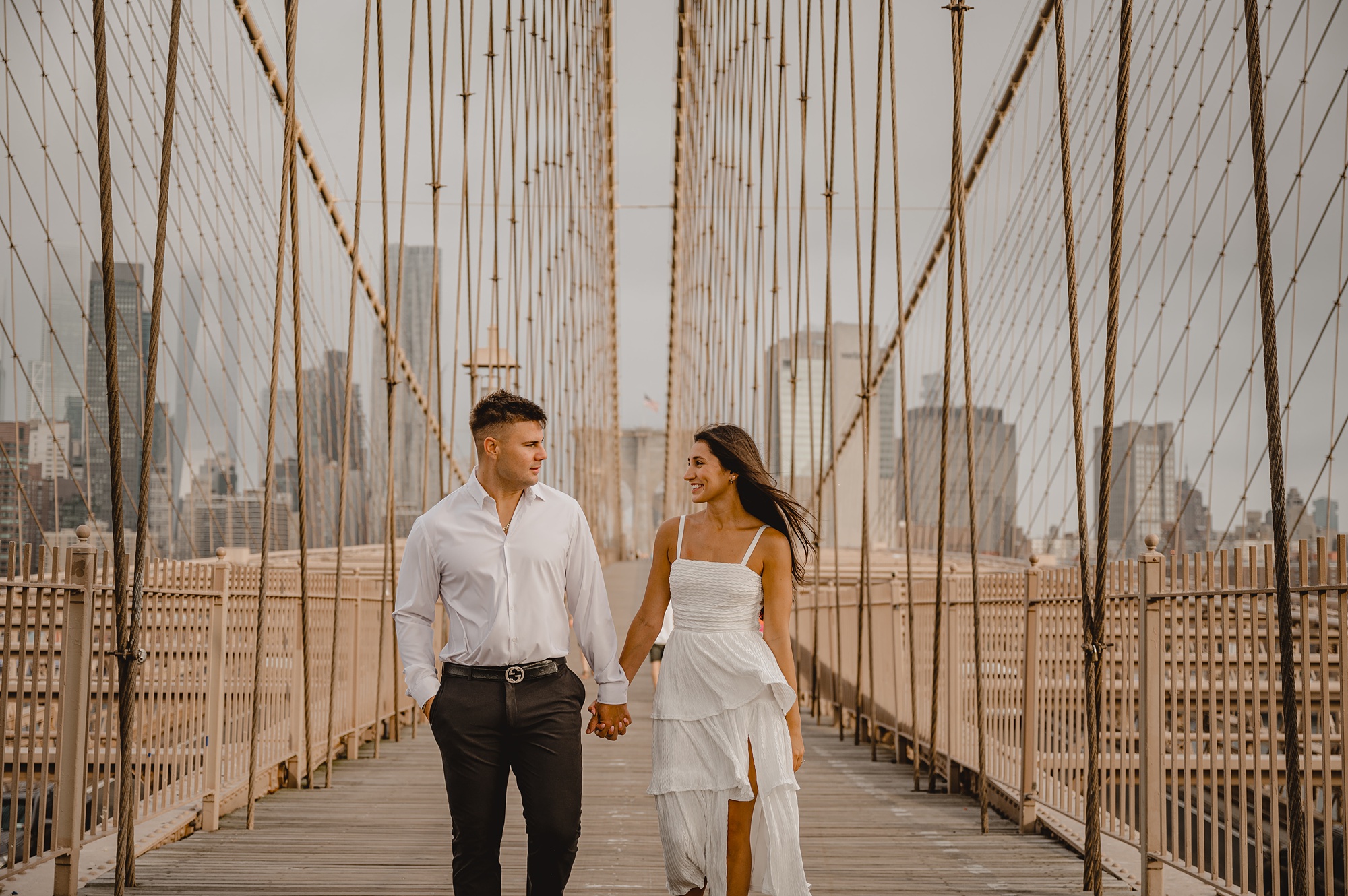 man and woman hold hands walking on the Brooklyn Bridge