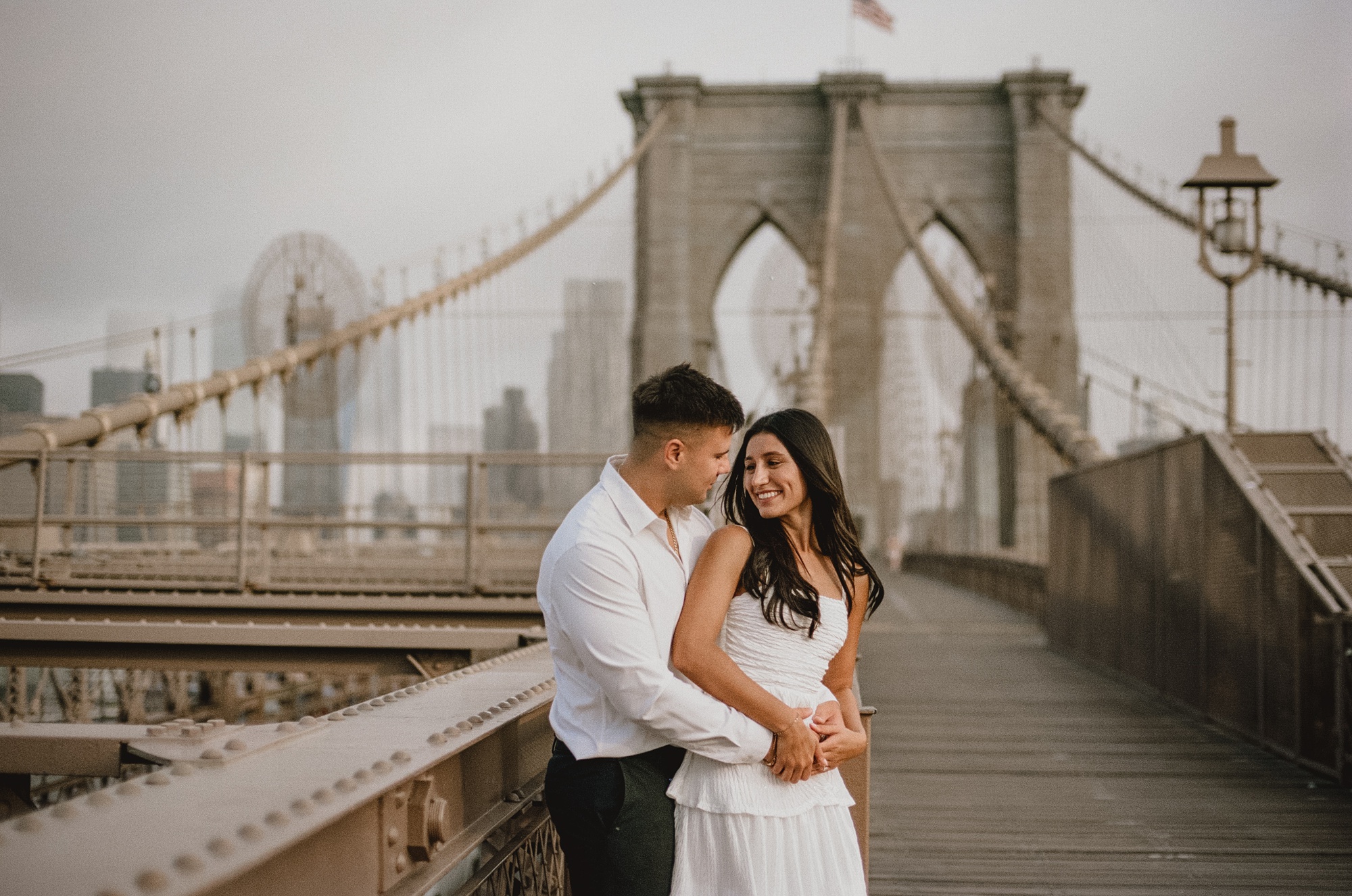 engaged couple hugs on the Brooklyn Bridge during photos in New York City