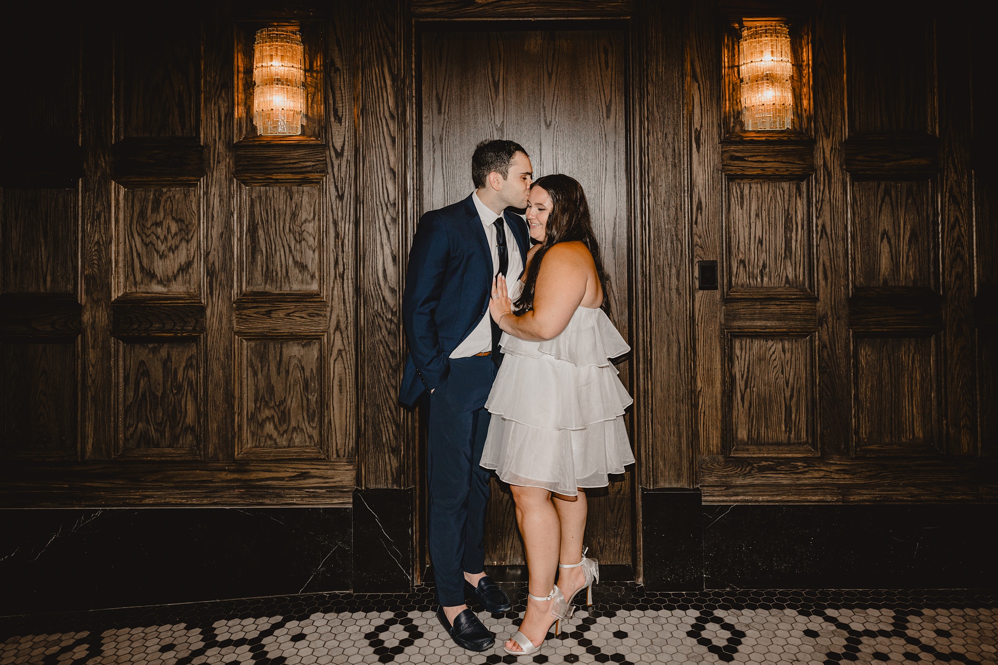 man and woman kiss in front of wood wall at the Beekman Hotel