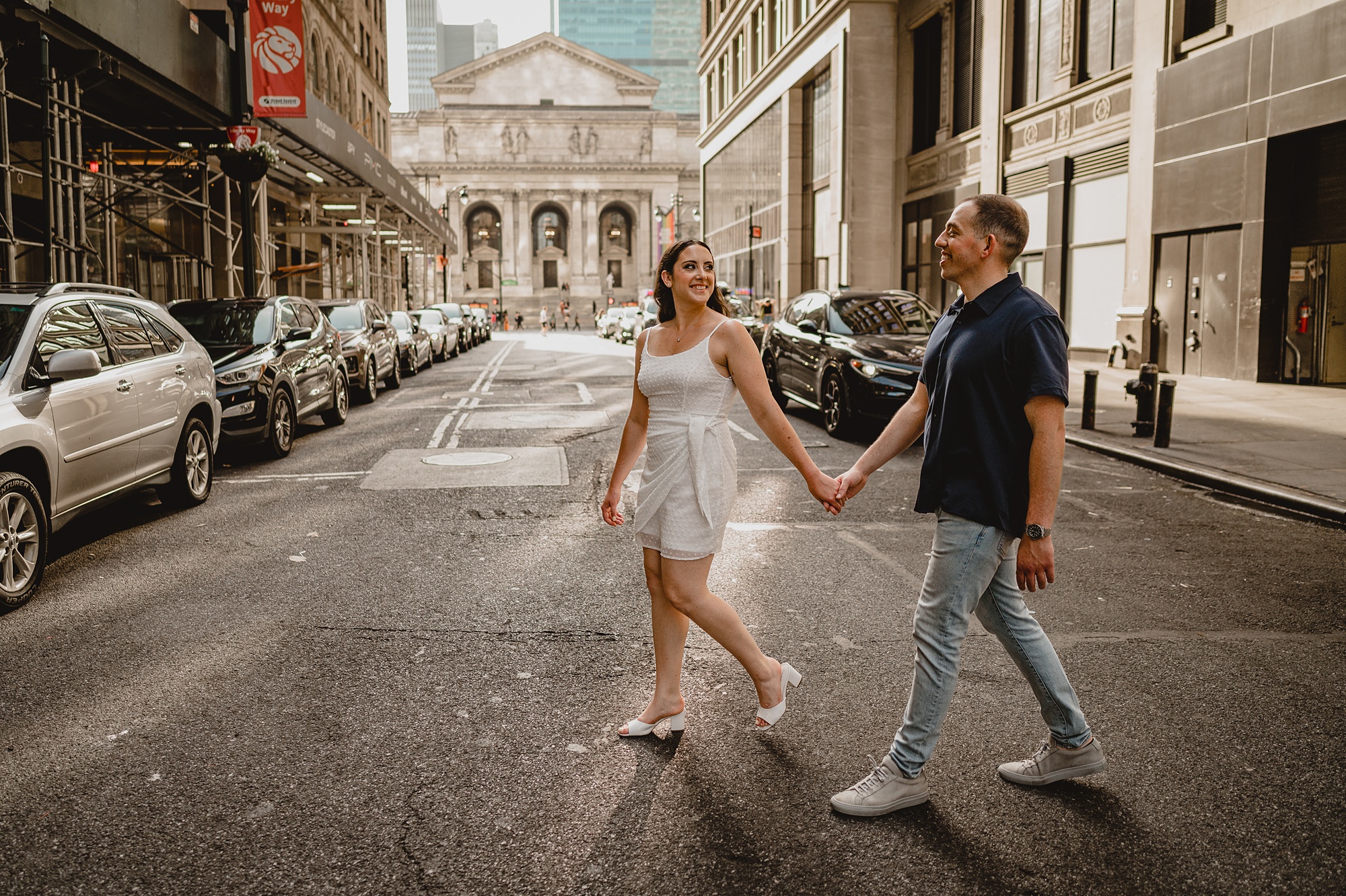 engaged couple holds hands walking across street near the New York Public Library