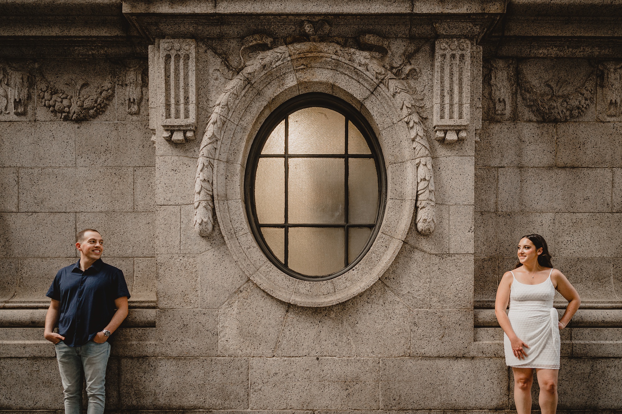 man and woman pose outside window of the New York Public Library