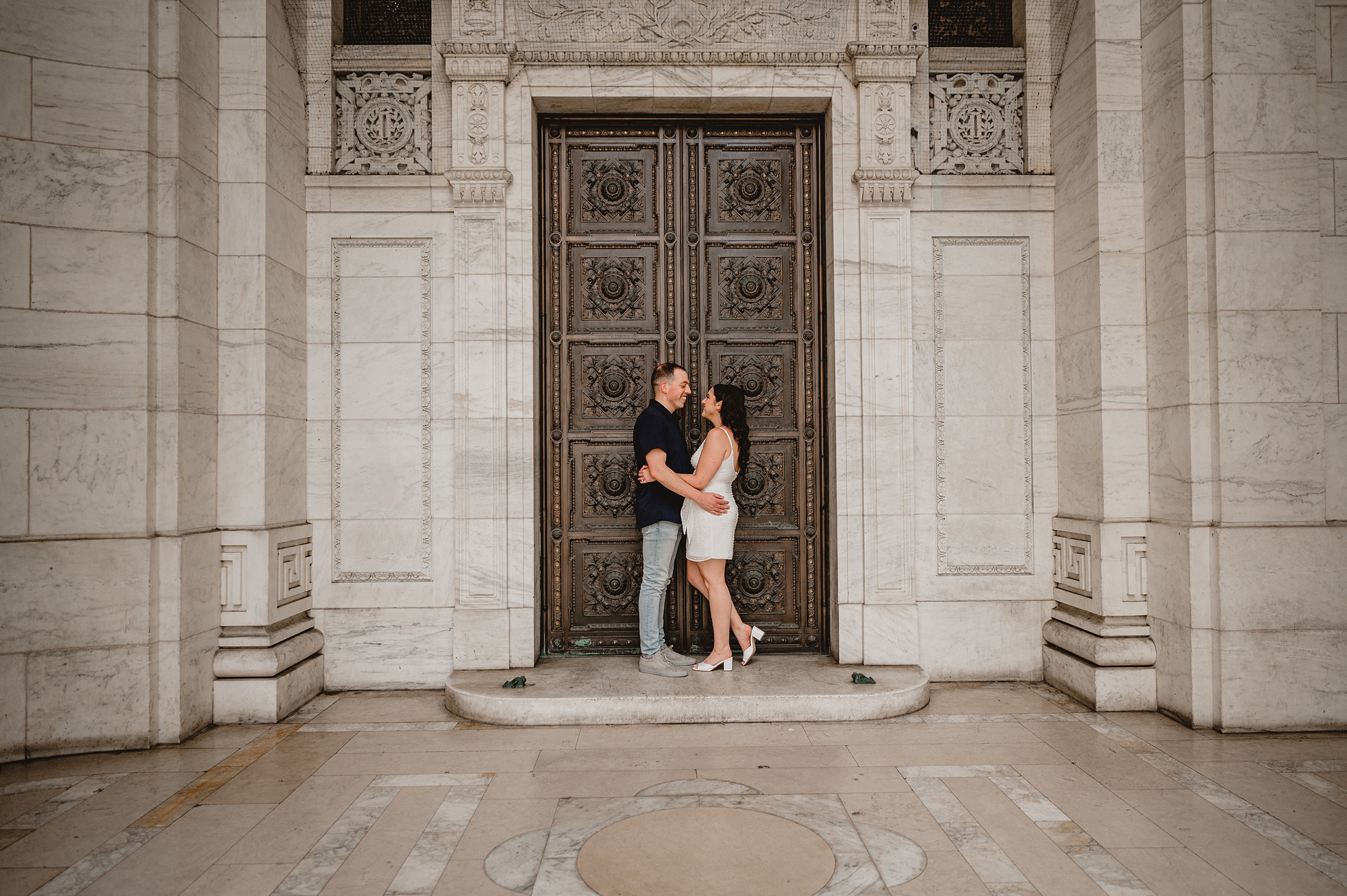 engaged couple pose in front of brown door of the New York Public Library