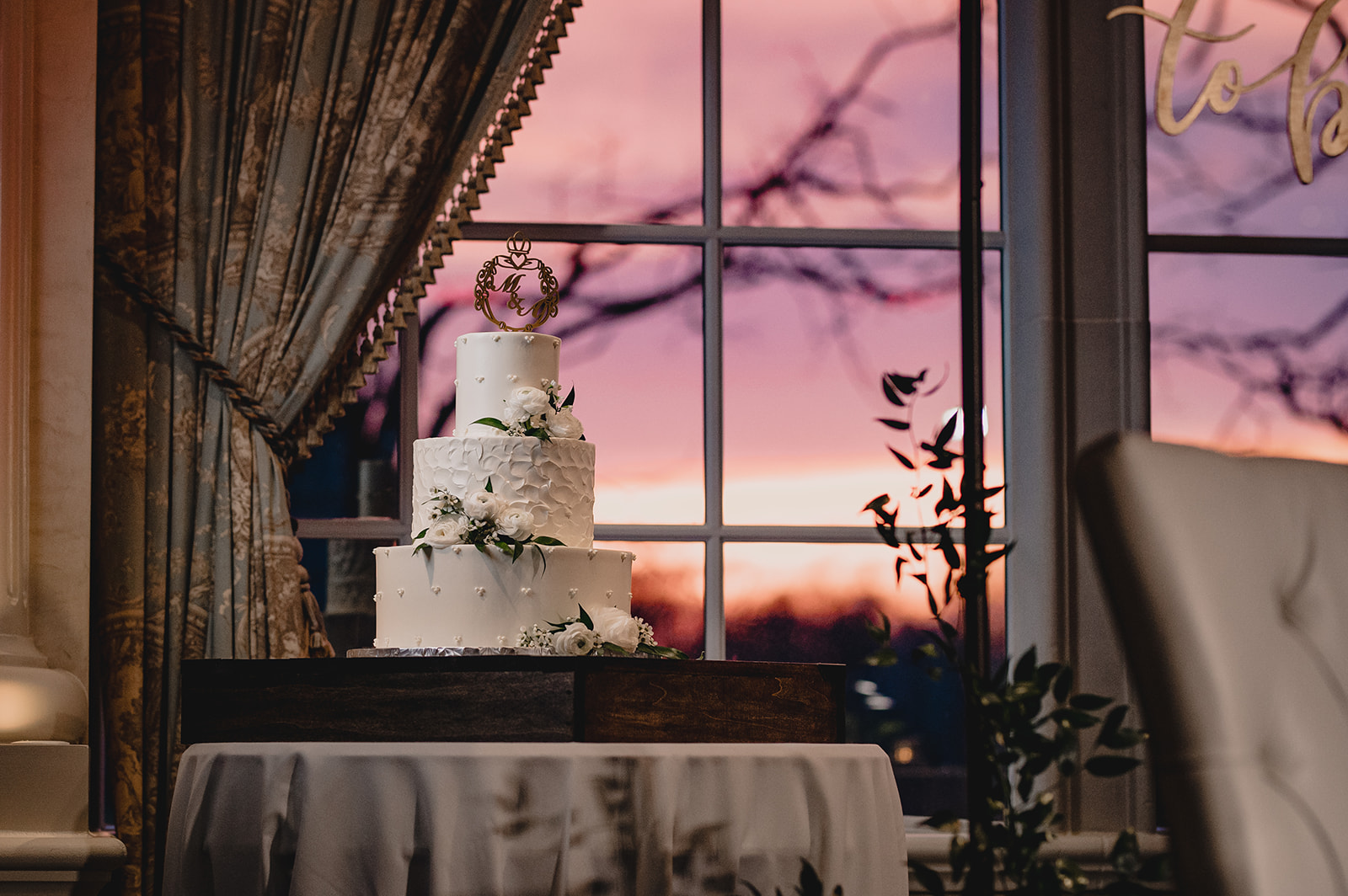 tiered wedding cake sits in front of window and sunset at Ashford Estate