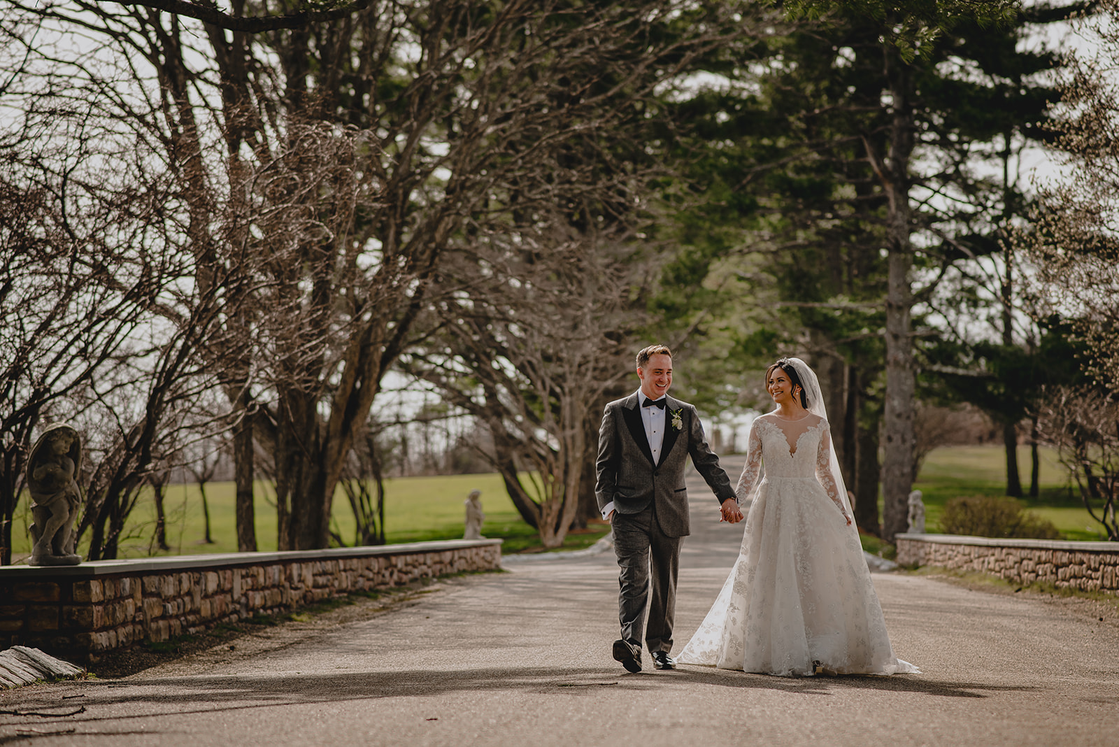 bride and groom hold hands walking on driveway with stone wall