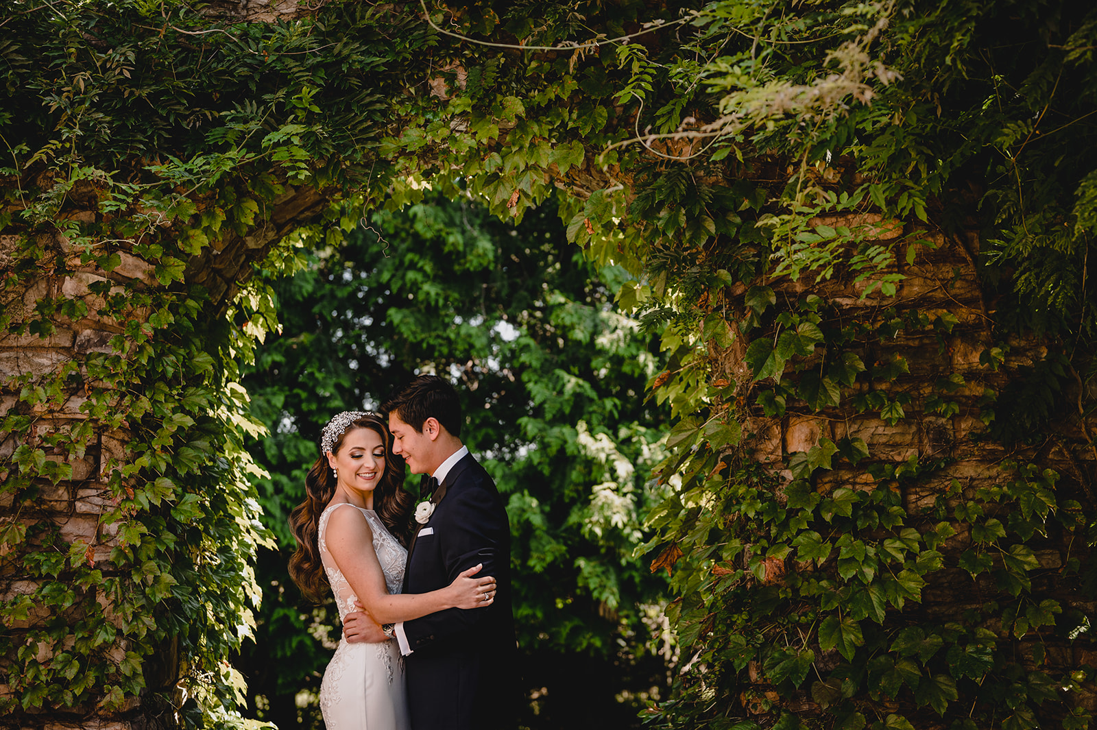 groom nuzzles bride's cheek in opening of stone wall covered in ivy