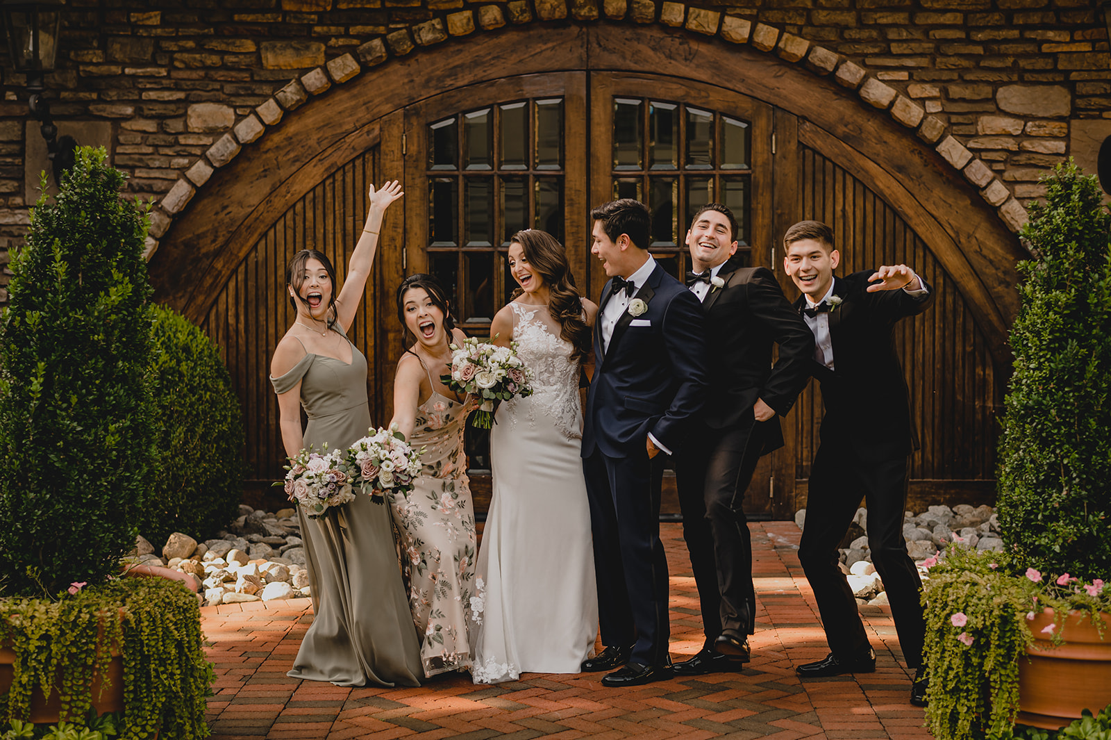 bride and groom laugh with wedding party outside wooden doors of the barn at Ashford Estate