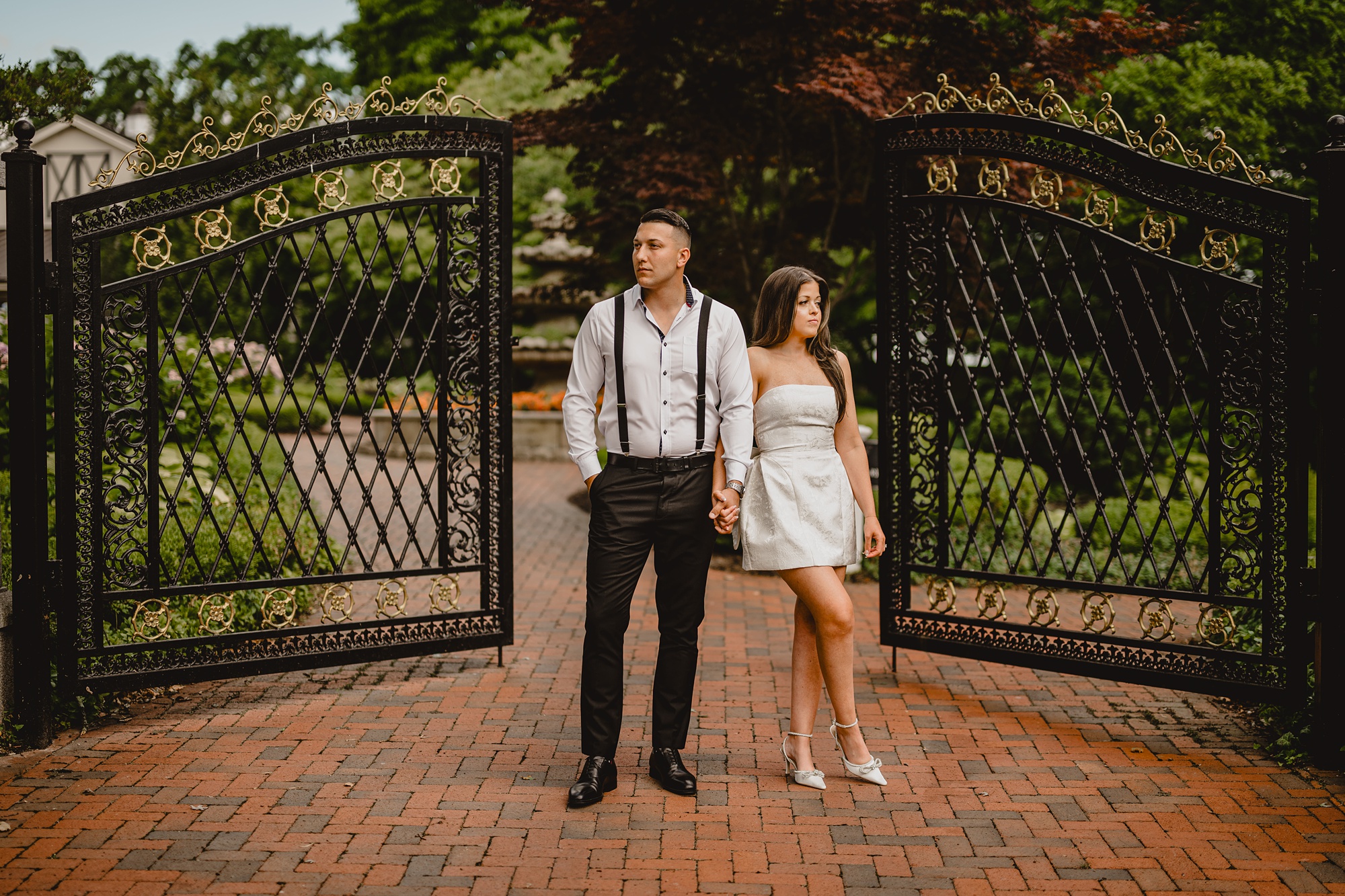 man and woman hold hands leaning away from each other by wrought iron gate at the Ashford Estate