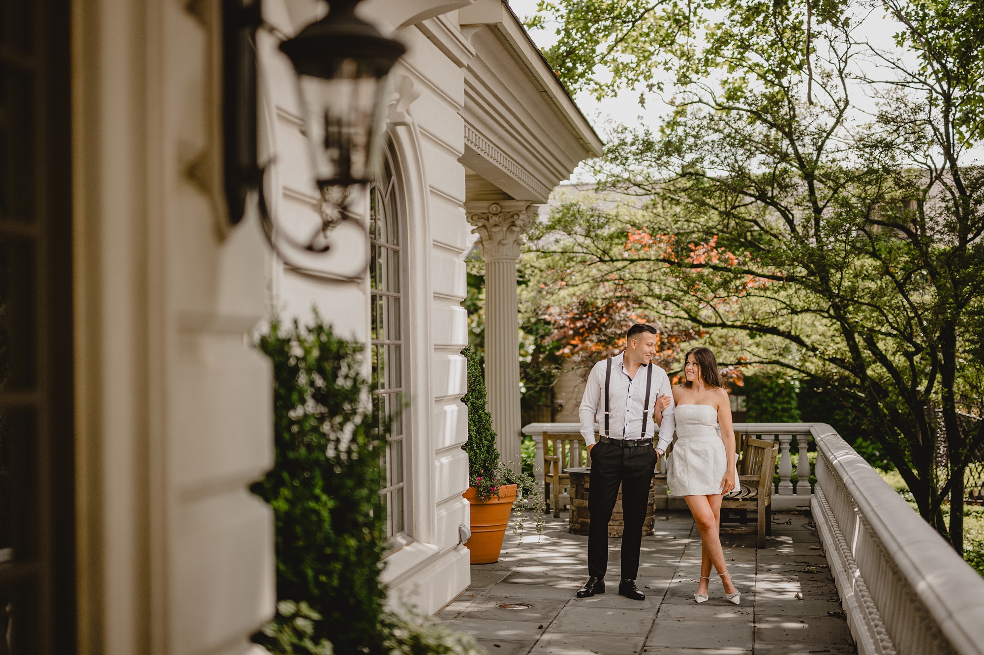 woman in short white dress holds man's hand on patio of the Ashford Estate