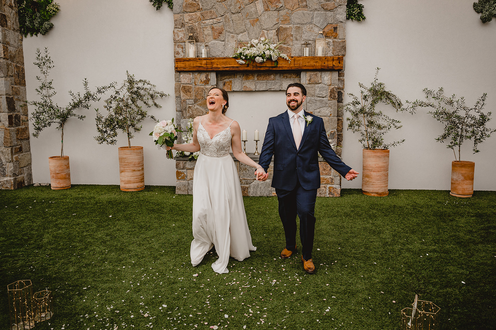 married couple holds hands laughing and walking away from stone fireplace 