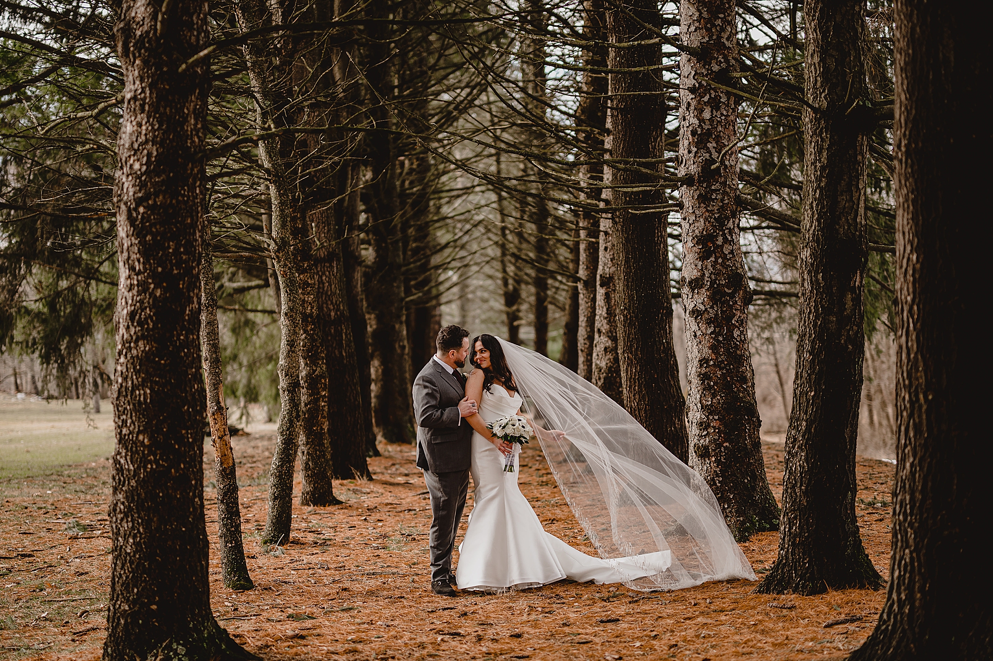 man and woman kiss between trees at the Reserve at Perona Farms