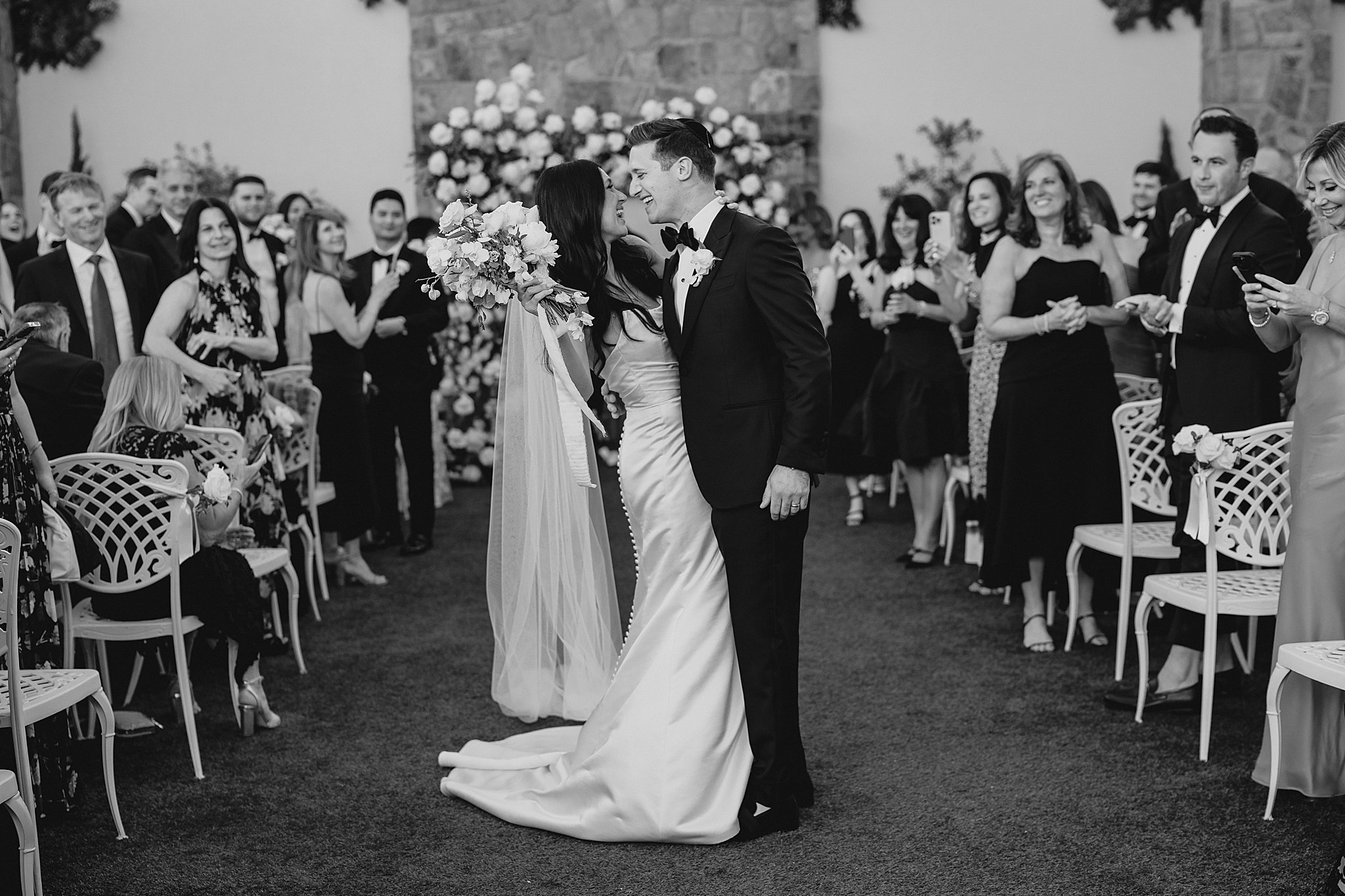 man and woman kiss on stone patio by fireplace during ceremony at the Reserve at Perona Farms