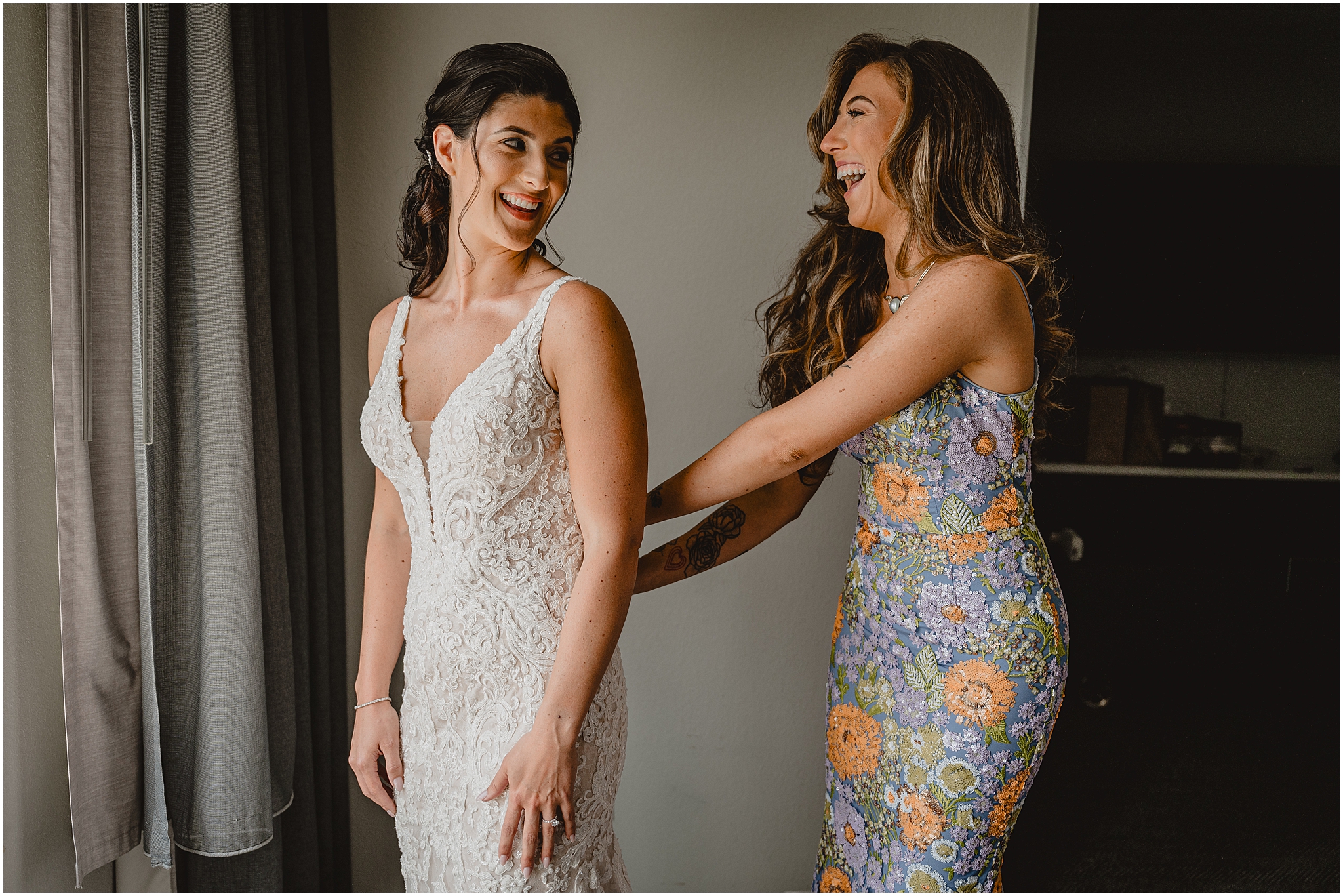 bridesmaid in floral dress helps bride into wedding dress at the Conservatory in New Jersey