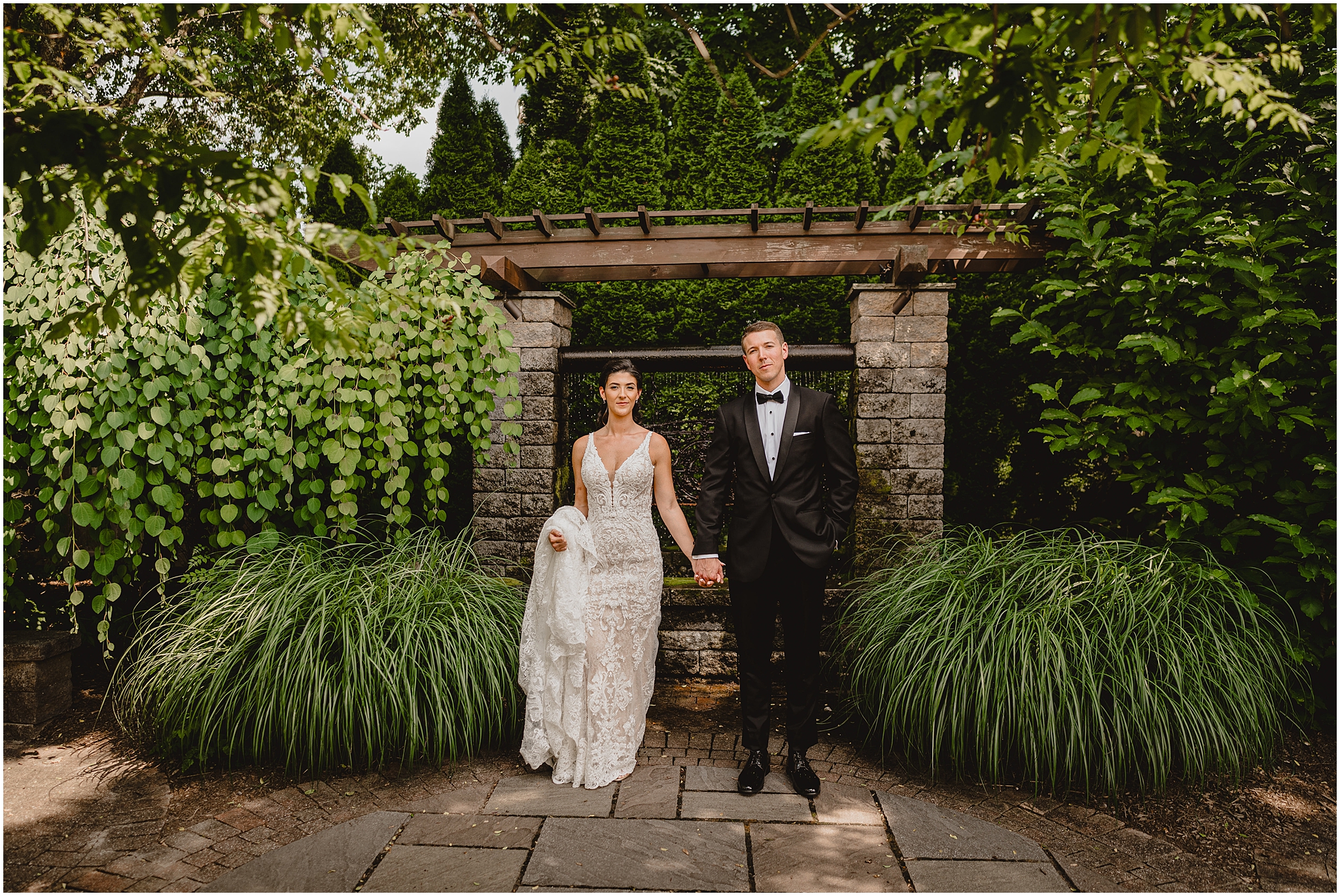 bride and groom stand in front of stone arbor on grounds at the Conservatory at Sussex County Fairgrounds