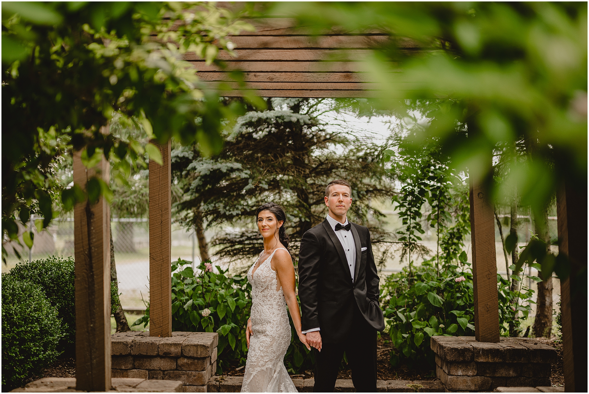 bride and groom hold hands under wooden arbor in the gardens