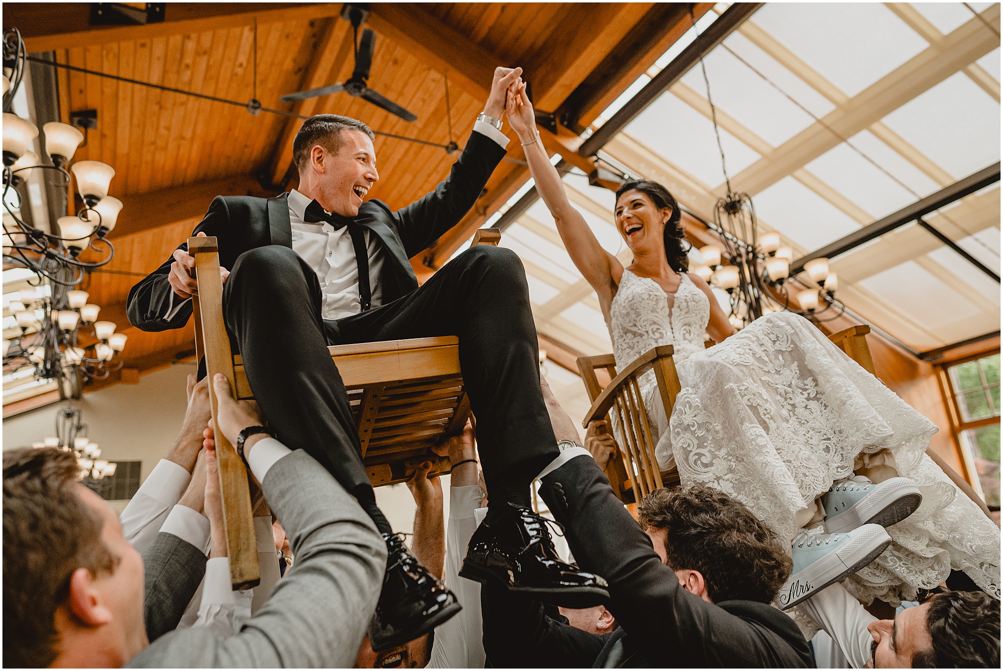 guests lift up bride and groom in chairs during hora at reception at the Conservatory at Sussex County Fairgrounds