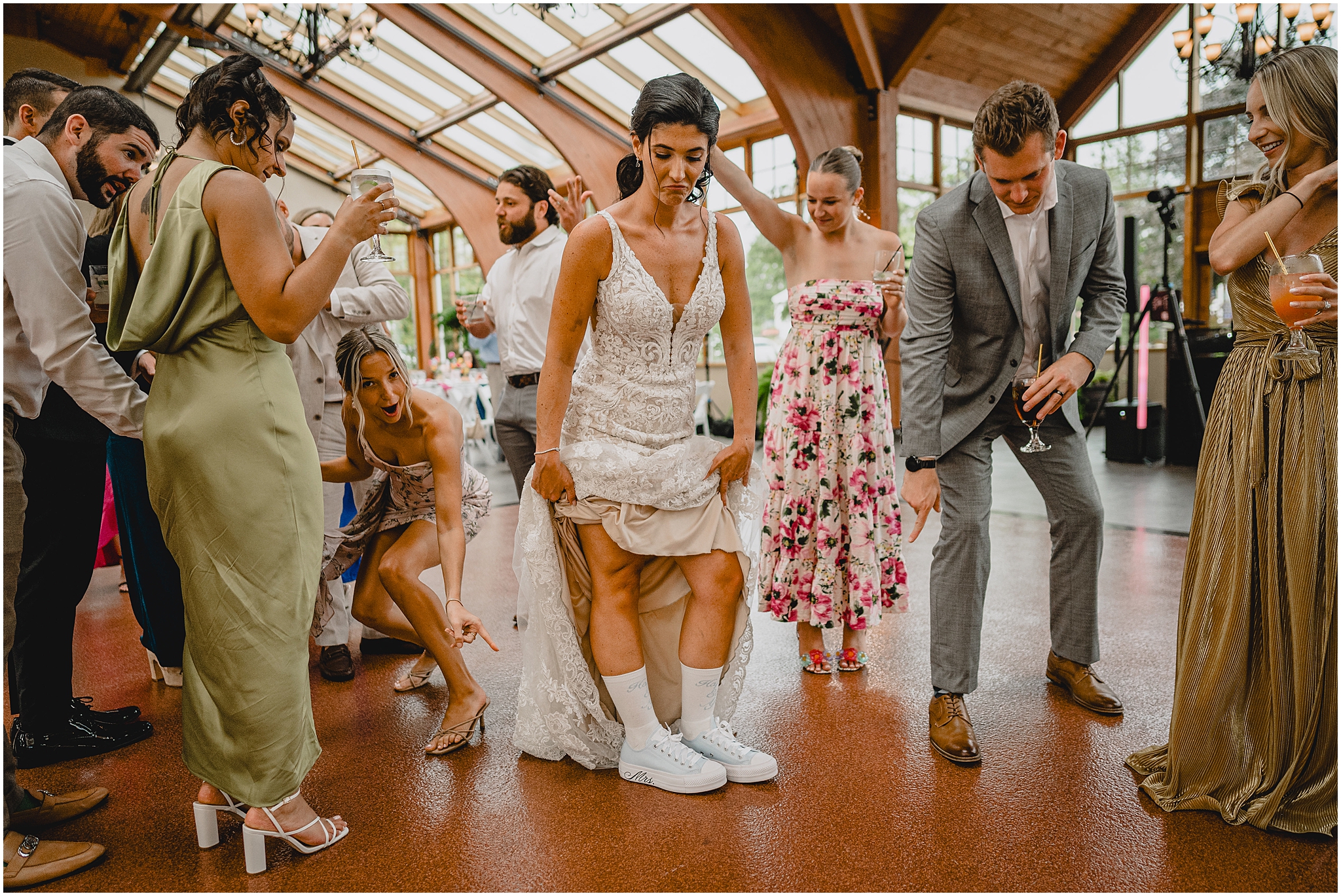 bride holds up wedding dress showing off white sneakers on dance floor