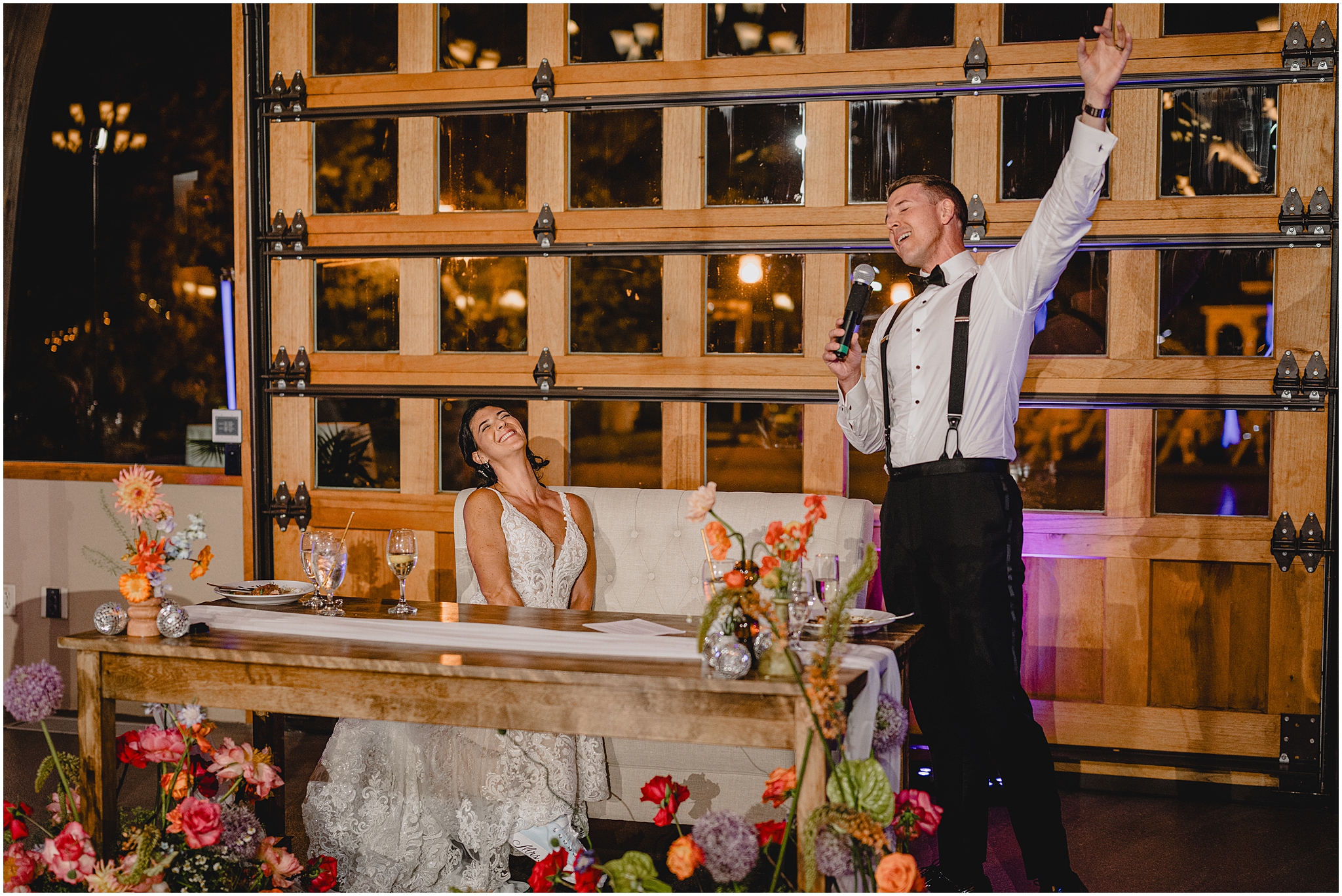 bride and groom laugh during toast sitting at wooden sweetheart table at the Conservatory