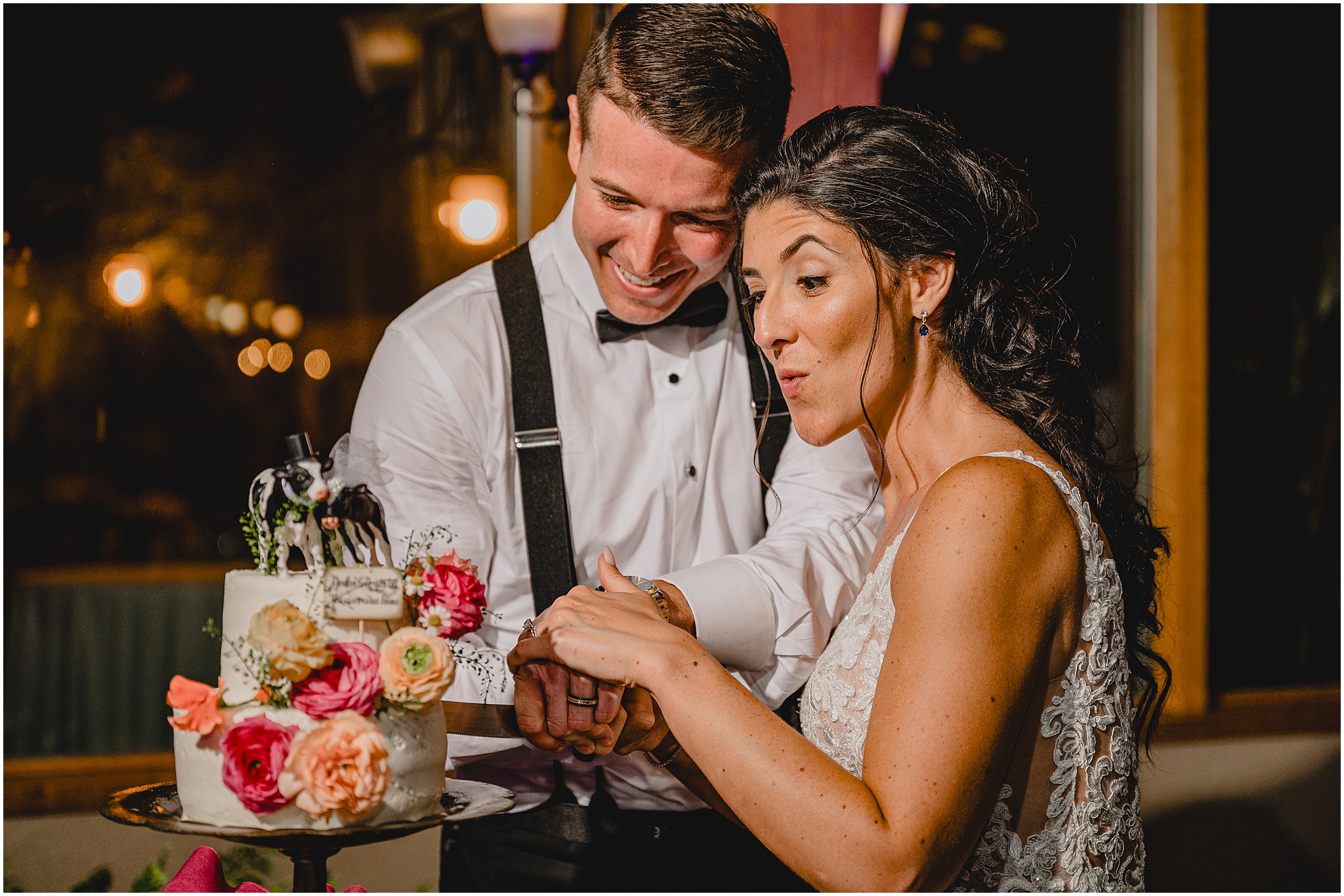bride and groom cut wedding cake with cow topper and peach and pink flowers 
