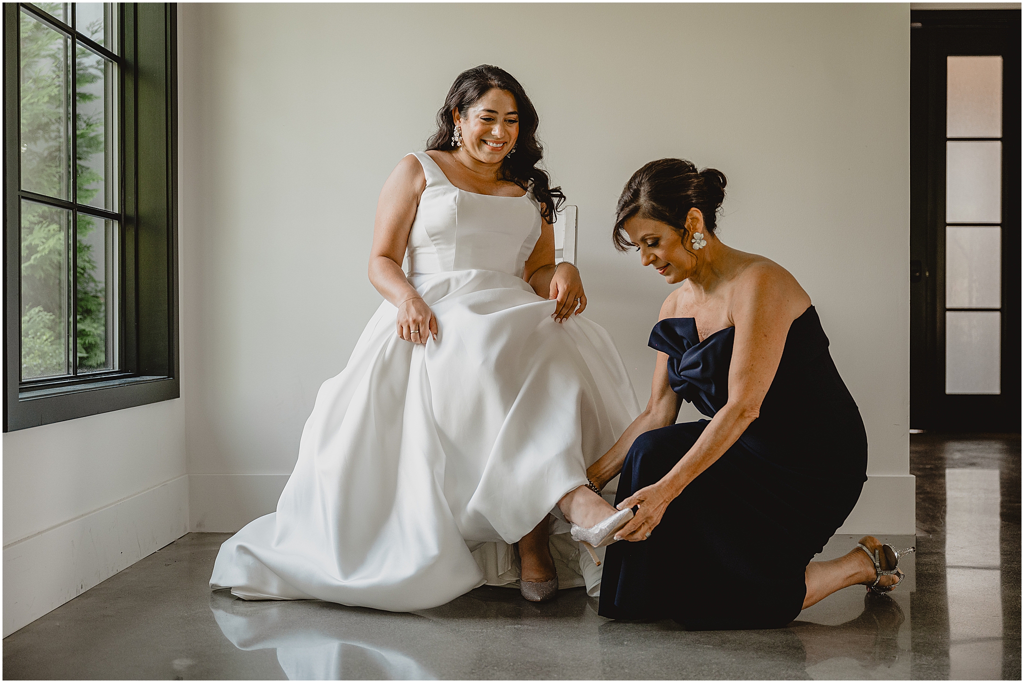 bridesmaid in navy blue dress kneels to help bride with ivory shoes
