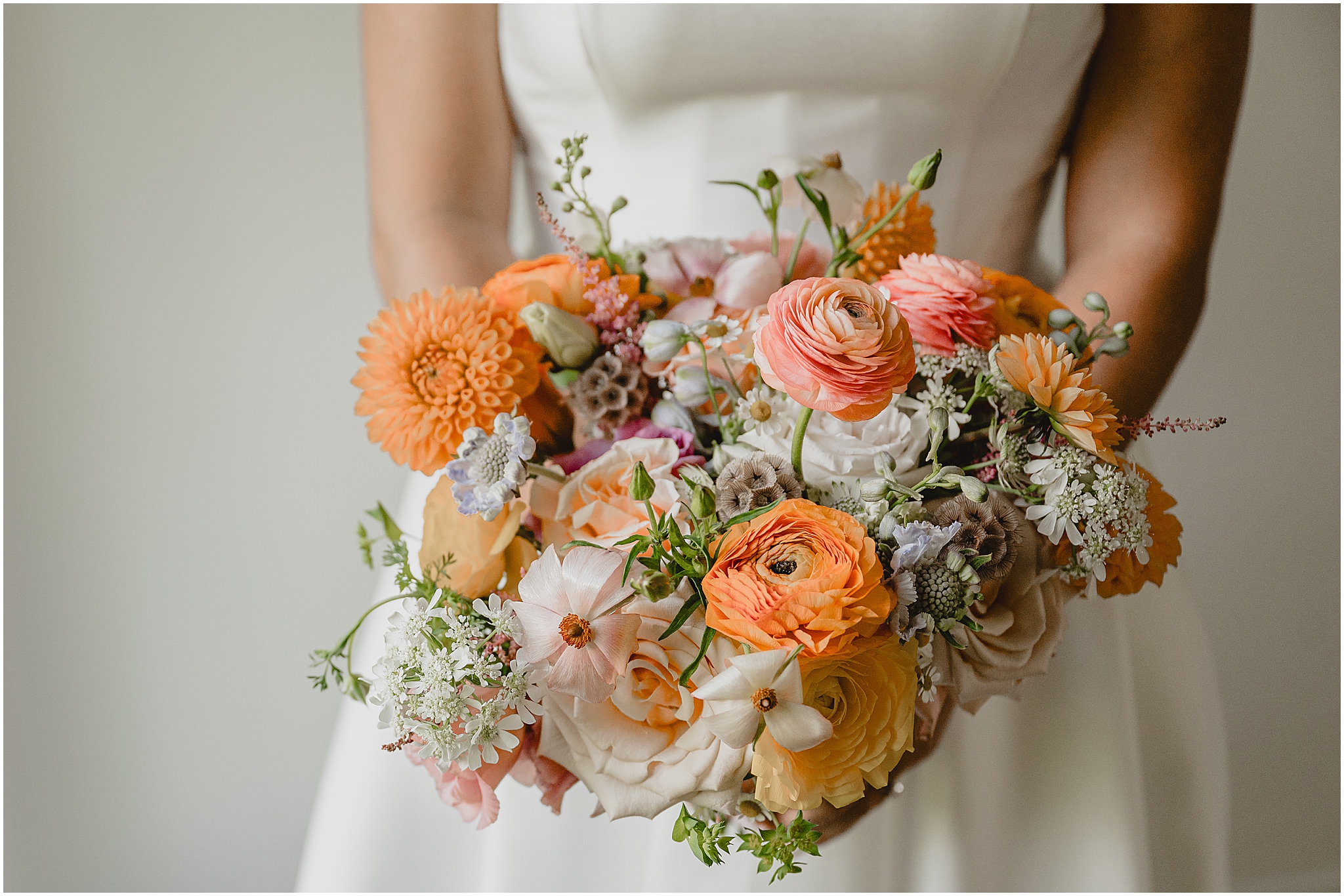bride holds bouquet of peach, pink, and orange flowers for summer wedding at the Perona Farms Refinery