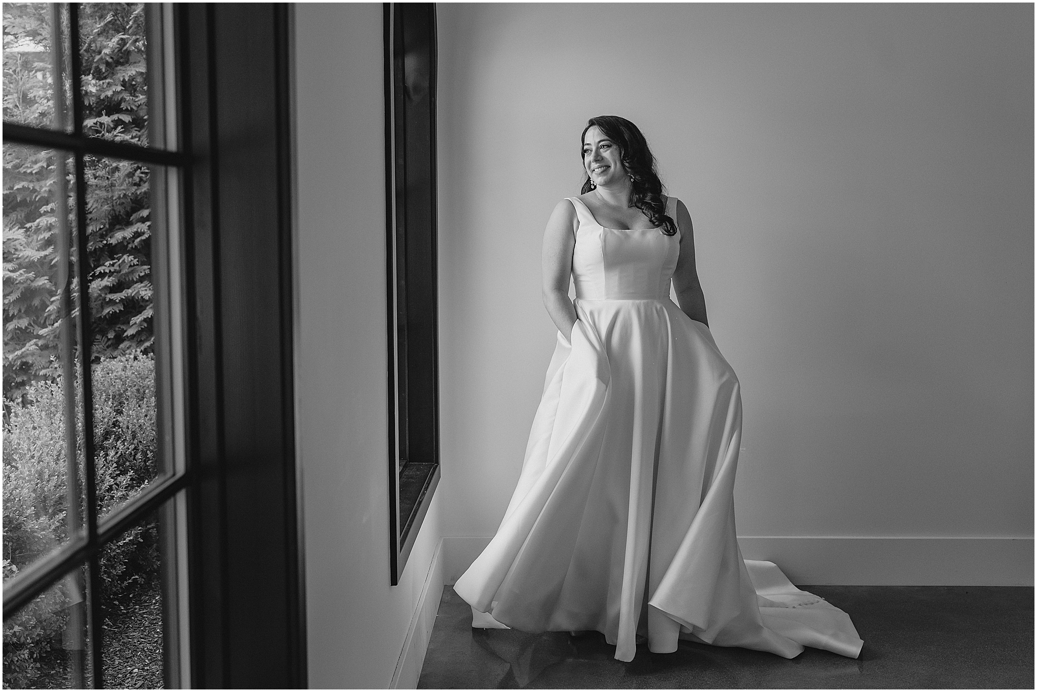bride stands with hands in pockets of wedding gown near windows at the Perona Farms Refinery