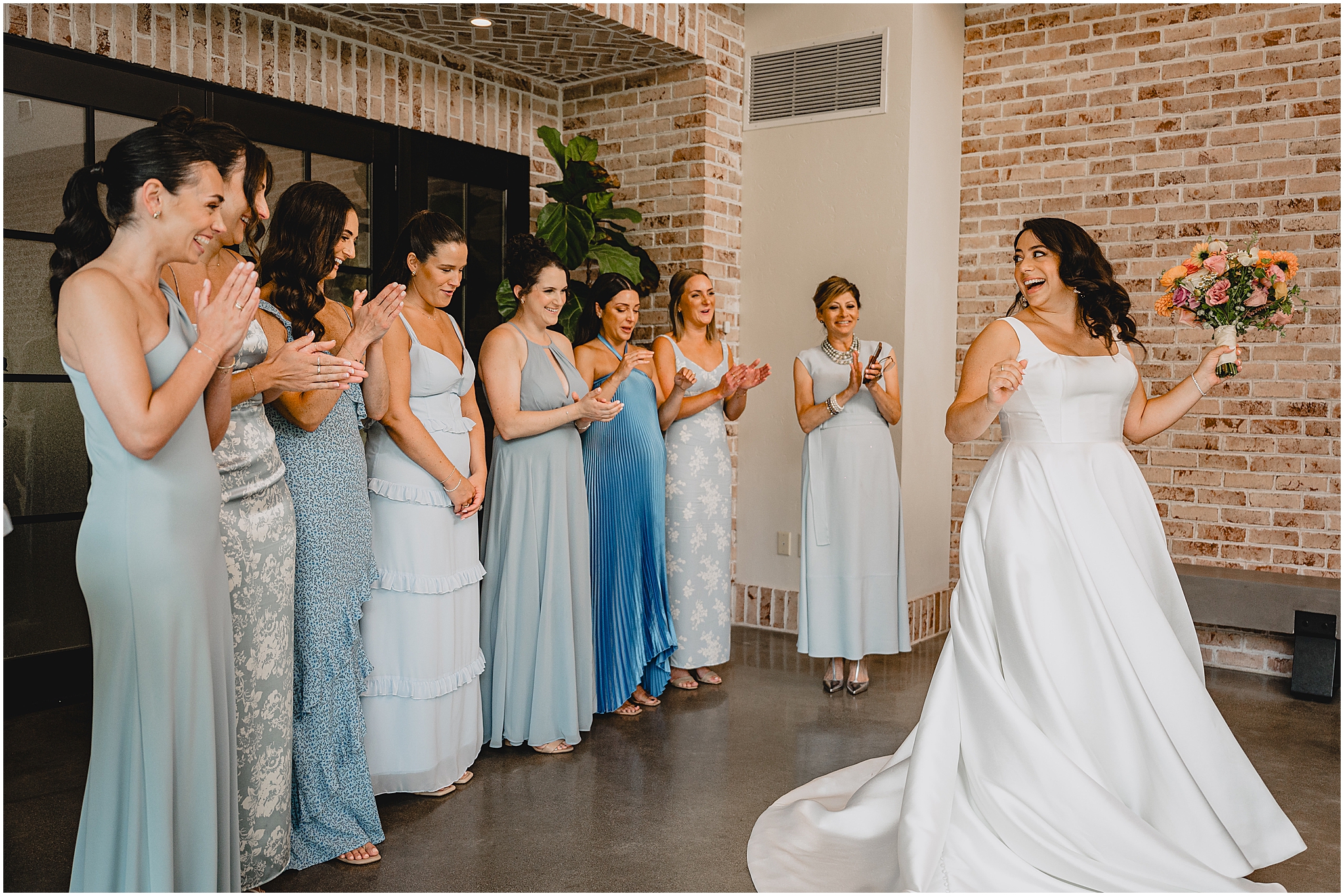 bridesmaids in mismatched light blue gowns have first look with bride twirling inside the Perona Farms Refinery