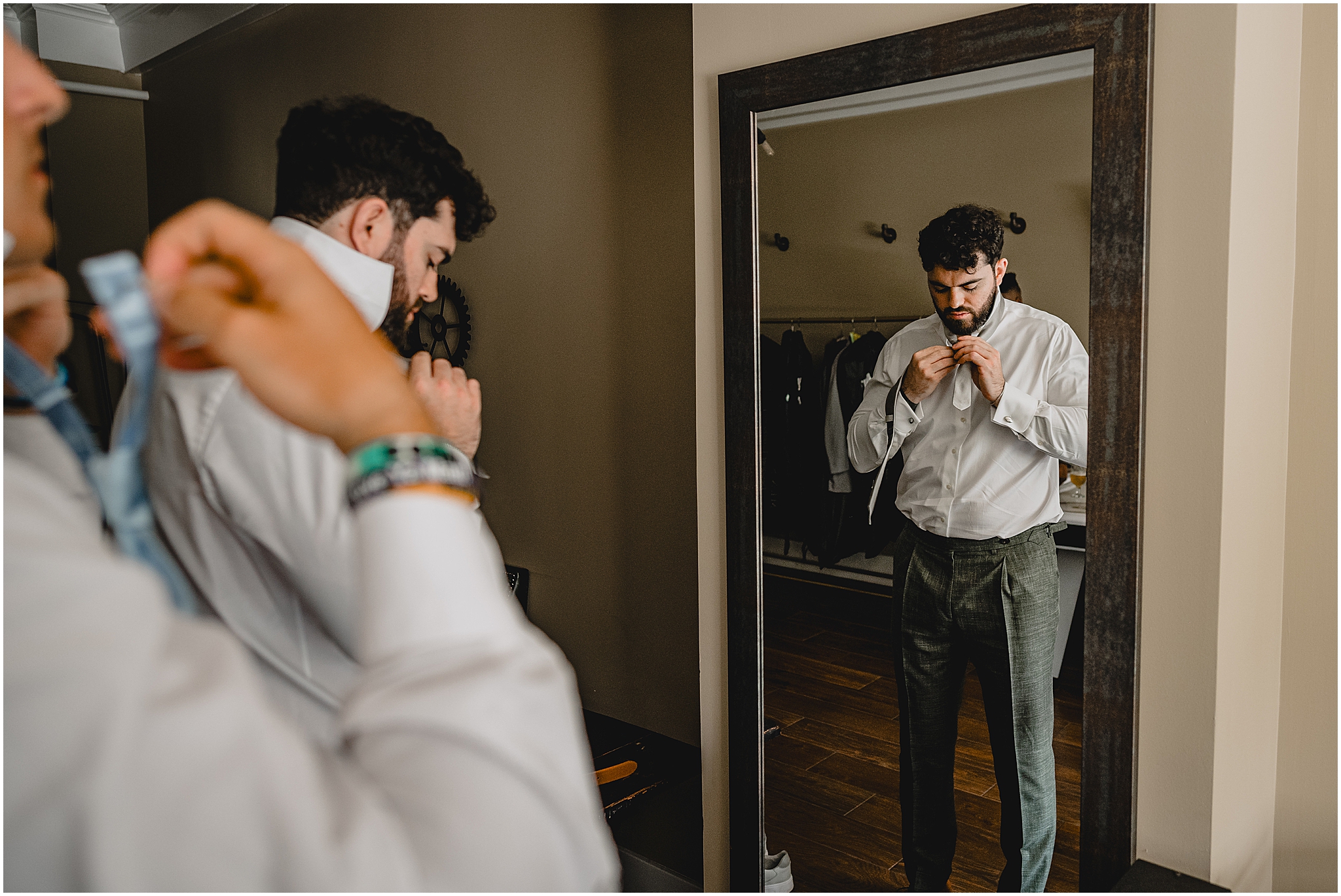 groom ties bowtie in mirror during summer wedding day prep