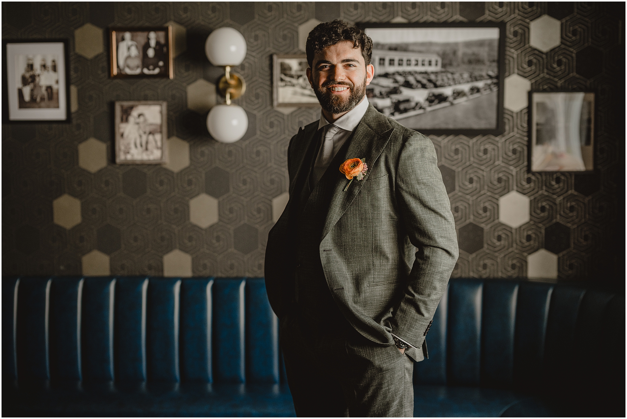 groom stands with hands in pocket of grey suit with bright coral boutonnière 