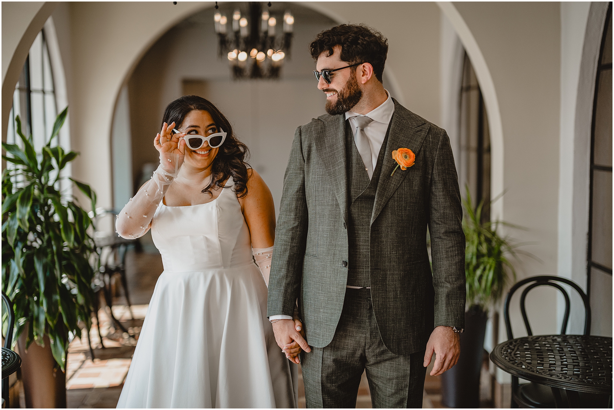 bride pulls white sunglasses down her nose smiling at the groom