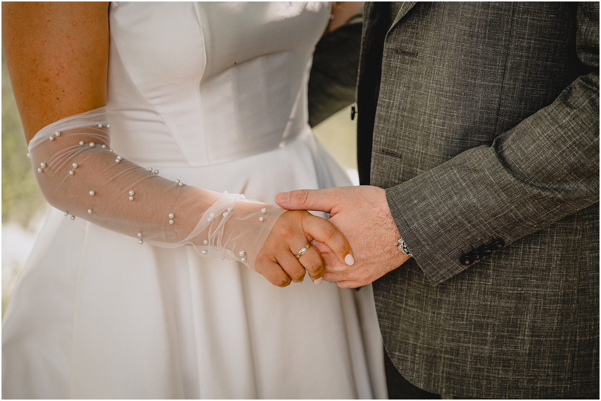 bride holds hands with groom wearing gauze and pearl sleeve
