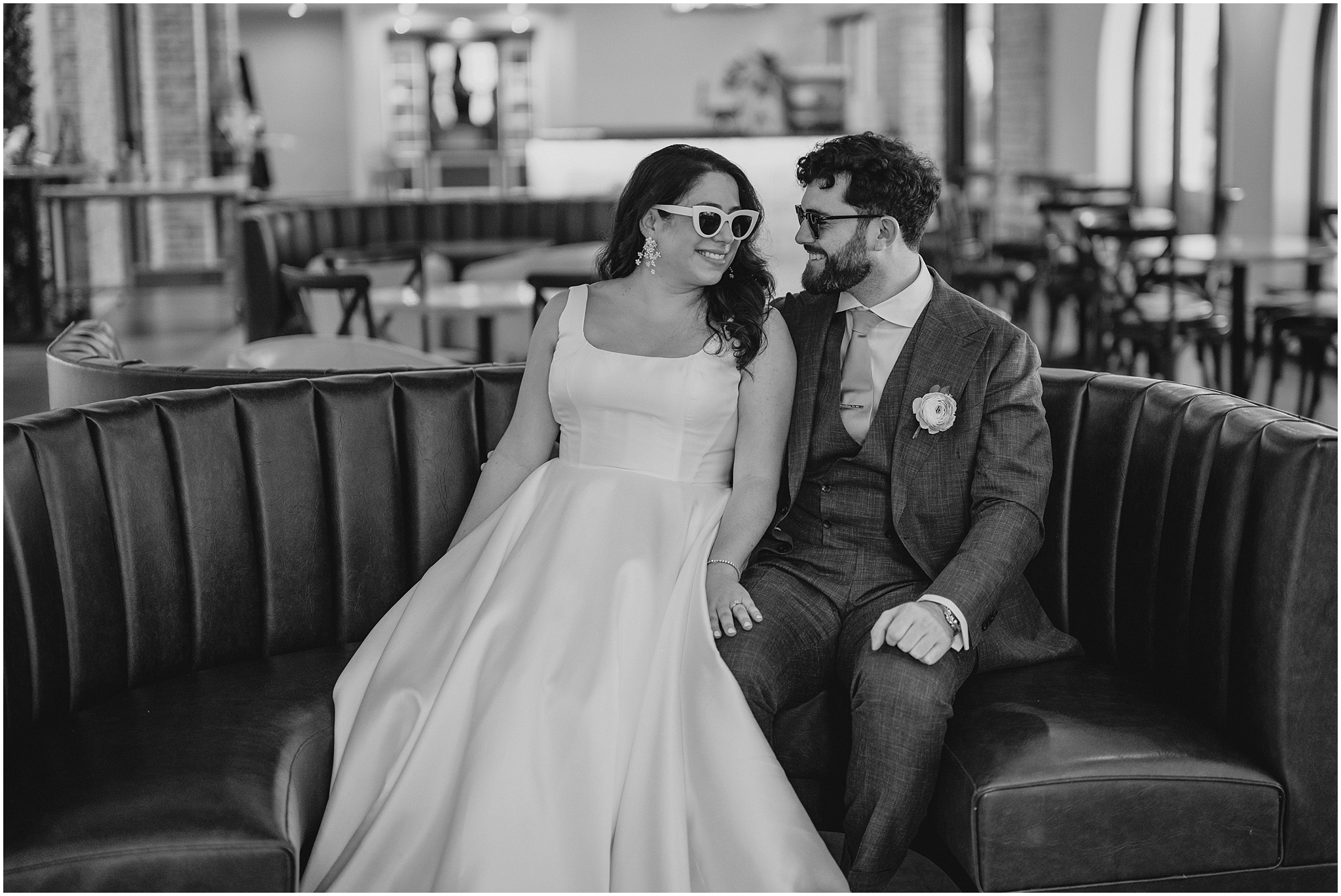 newlyweds sit together on leather couch during photos at the Perona Farms Refinery