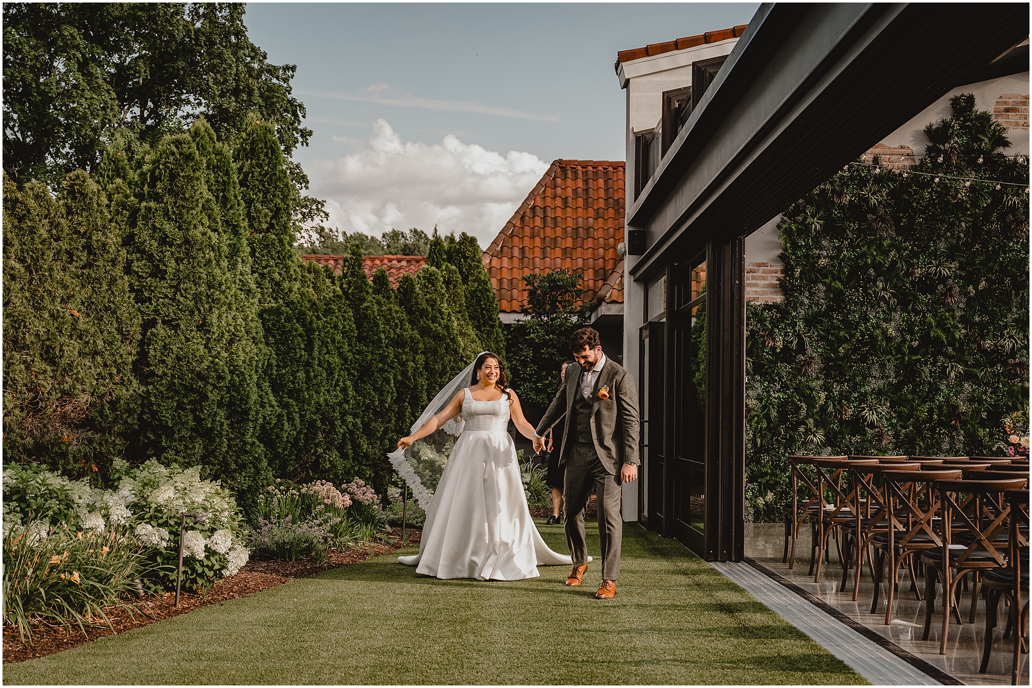 newlyweds hold hands walking by outdoor atrium in Andover NJ wedding venue
